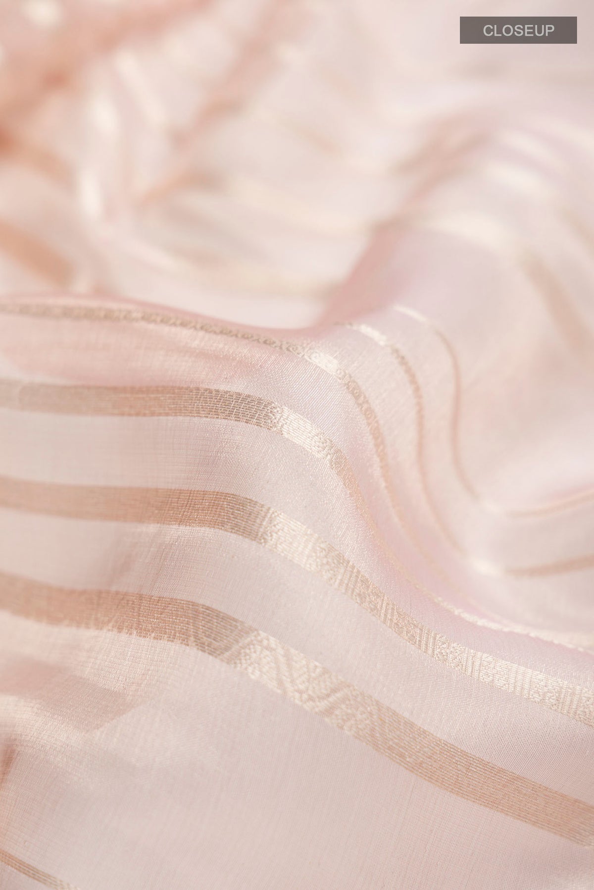 Close up of Pink Tissue Silk Saree with Stripes on the body and Zari Border displaying folds