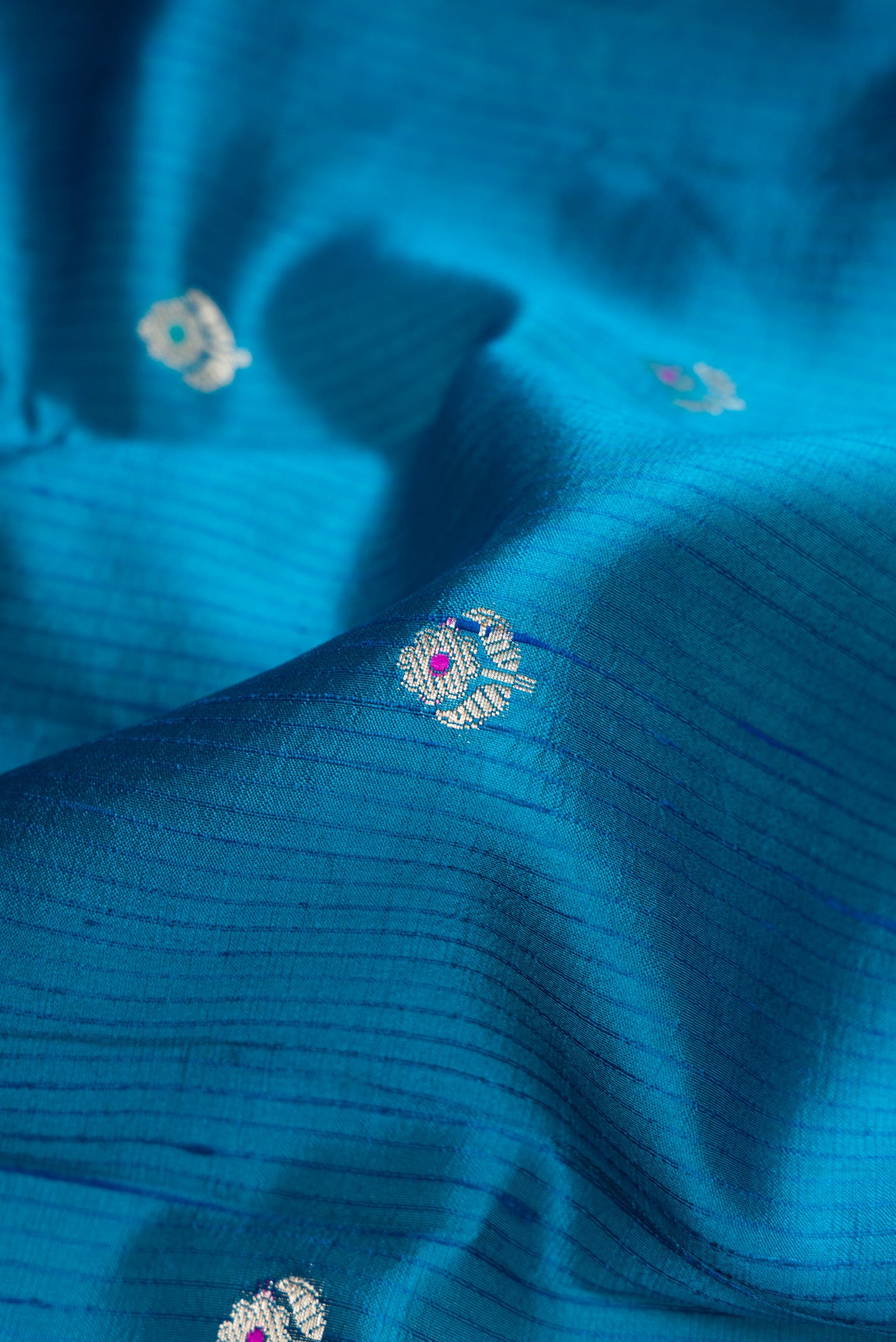 Close up of Peacock Blue Dual Tone Tussar Silk Saree with Zari Butta on the body and Zari Border.  displaying folds