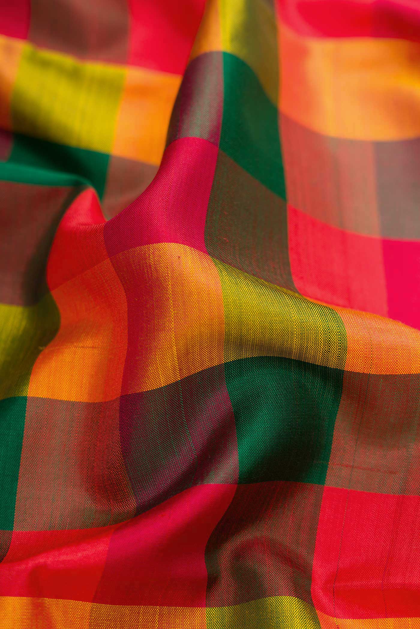 Close up of Red, Green and Orange Color Kanchipuram Silk Saree with Checked design on the body and Thread Border.  displaying folds