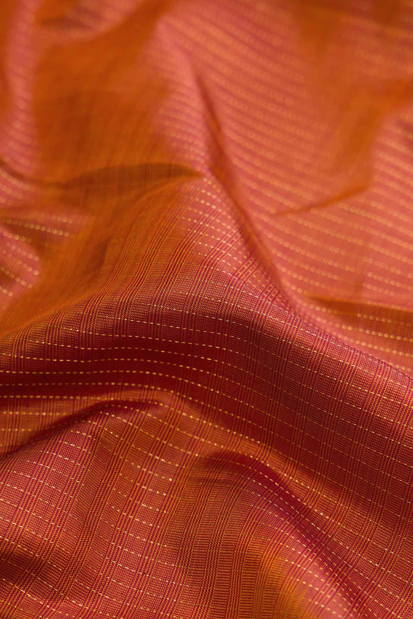 Close up of Brick Orange Dual Tone Kanchipuram Silk Saree with Stripes on the body and Zari Border displaying folds