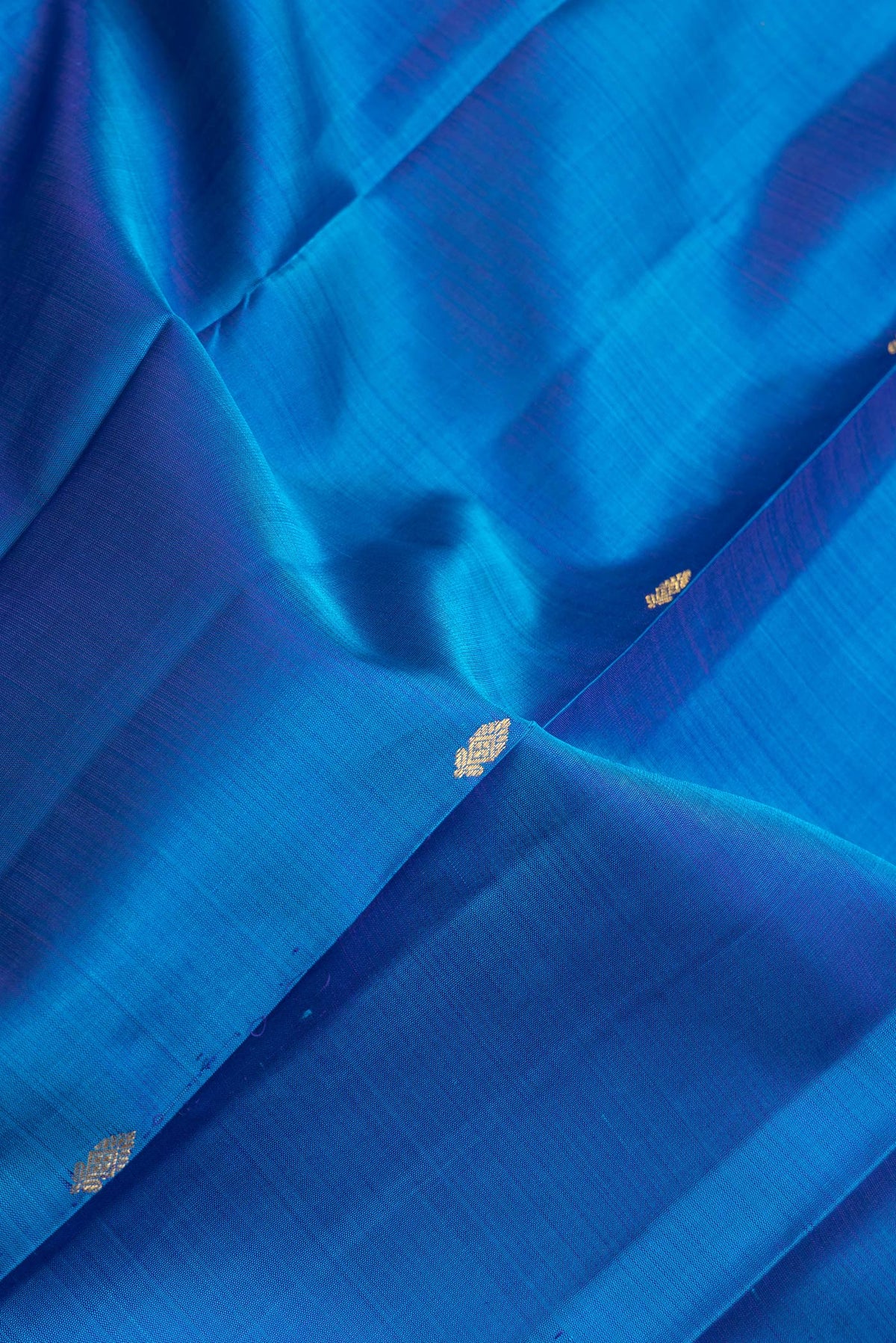 Close up of Peacock Blue Dual Tone Kanchipuram Silk Saree with Zari Butta on the body and Zari Border.  displaying folds