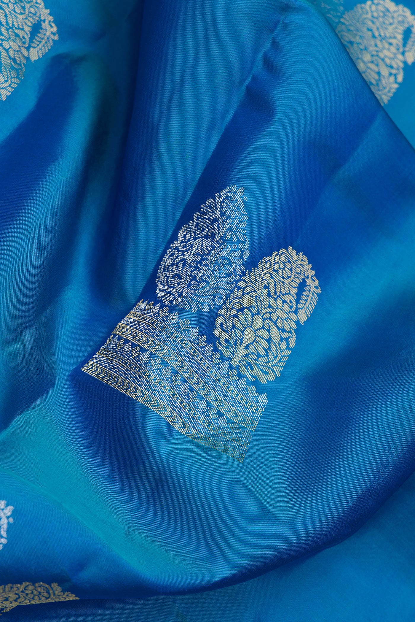 Close up of Peacock Blue Dual Tone Kanchipuram Silk Saree with Zari Butta on the body and Zari Border.  displaying folds