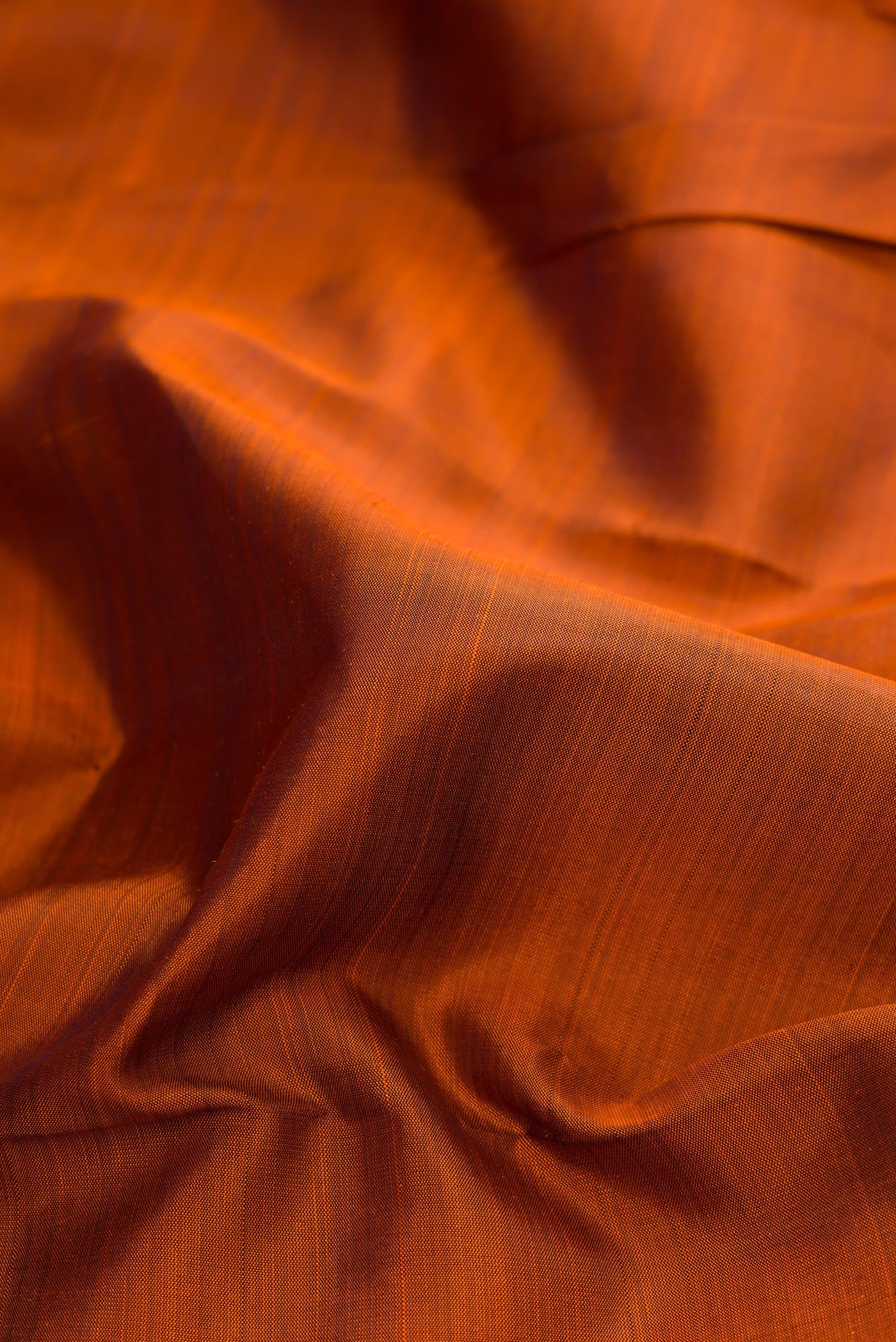 Close up of Brick Orange Dual Tone Kanchipuram Silk Saree with Plain Body and Rising Temple Border.  displaying folds