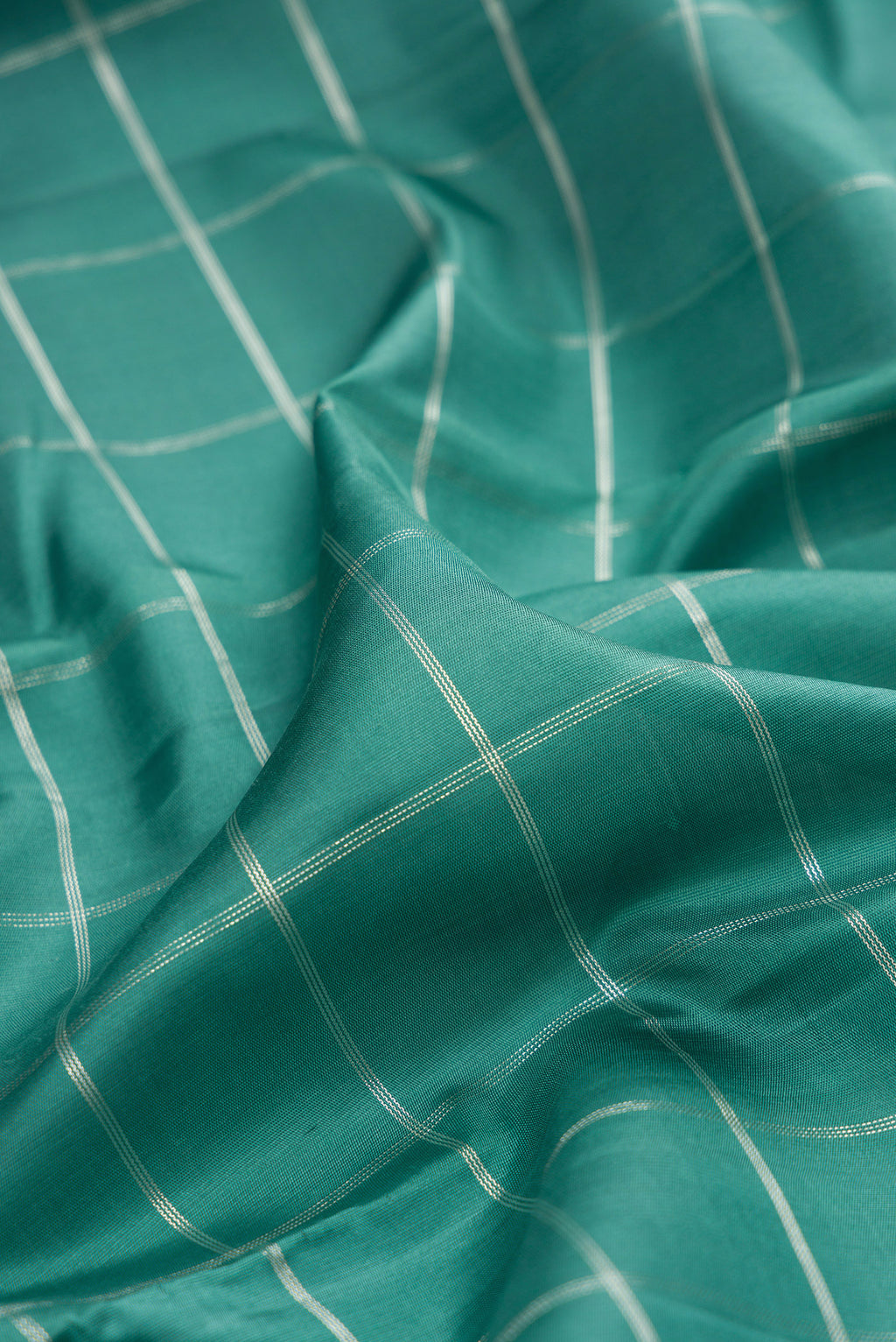Close up of Pure Silk Teal Kanchipuram Saree with Checked design on the body and Zari Border.  displaying folds