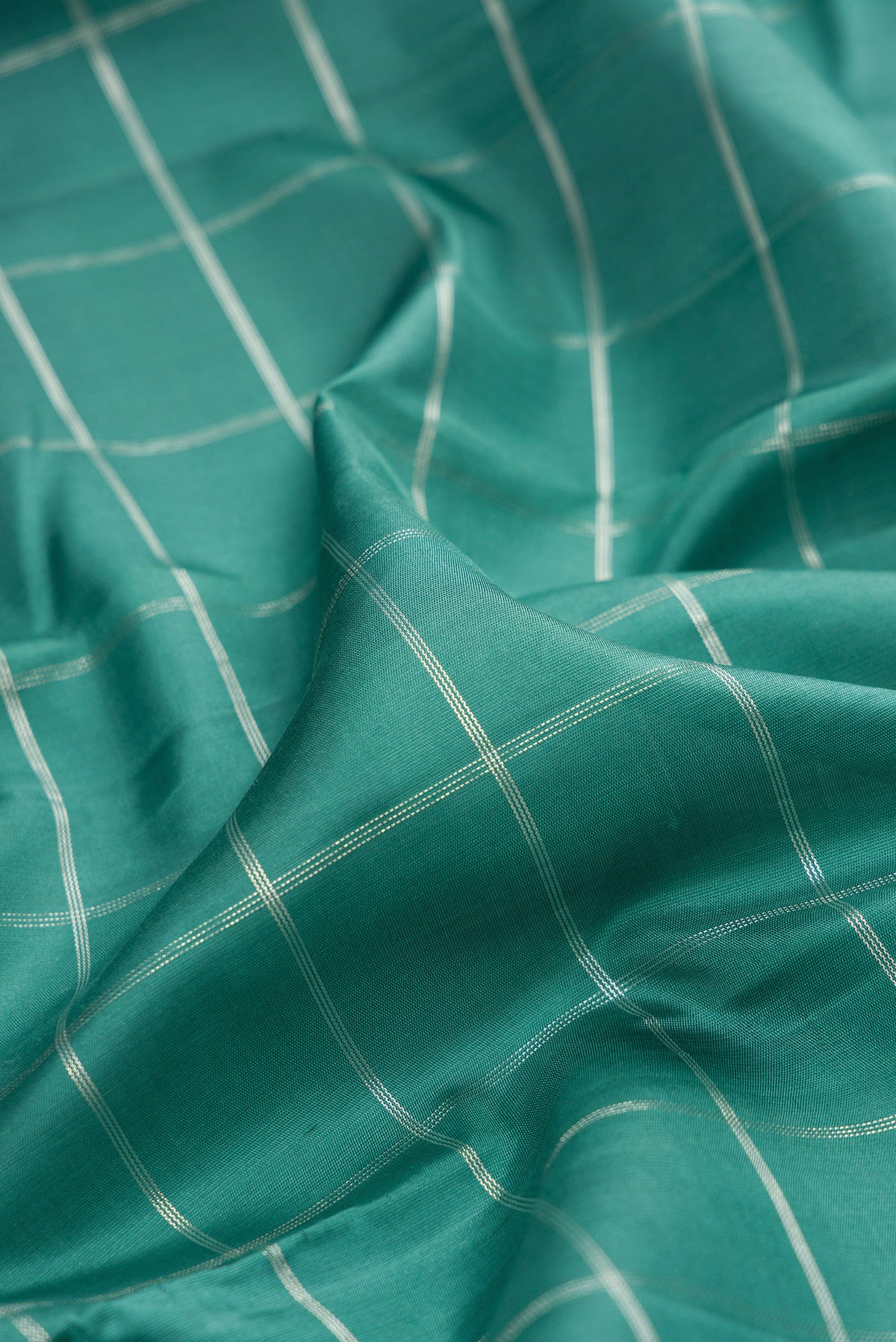 Close up of Pure Silk Teal Kanchipuram Saree with Checked design on the body and Zari Border.  displaying folds