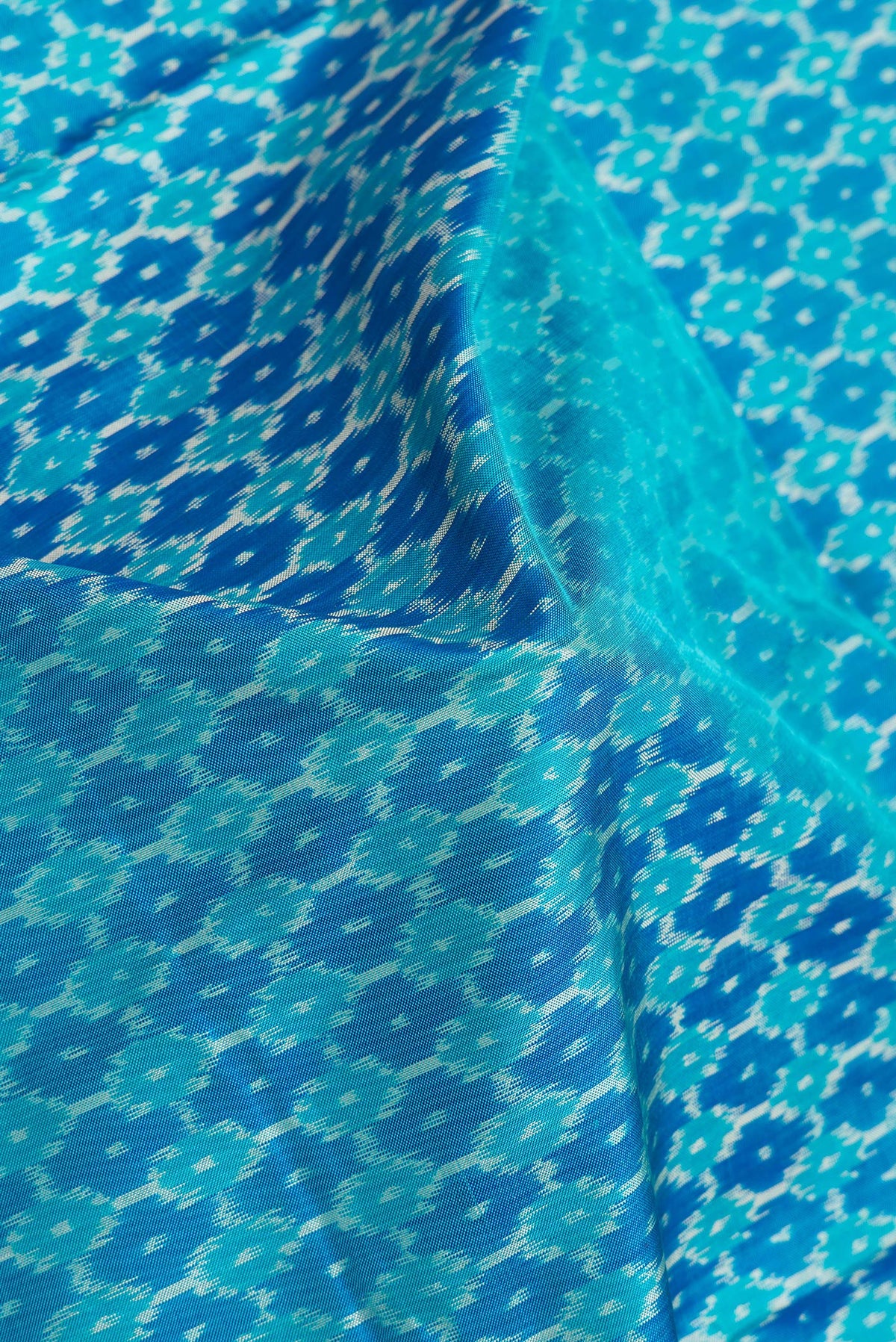 Close up of Sky Blue Dual Tone Double Ikat Saree with Ikat Print on the body and Plain Border.  displaying folds