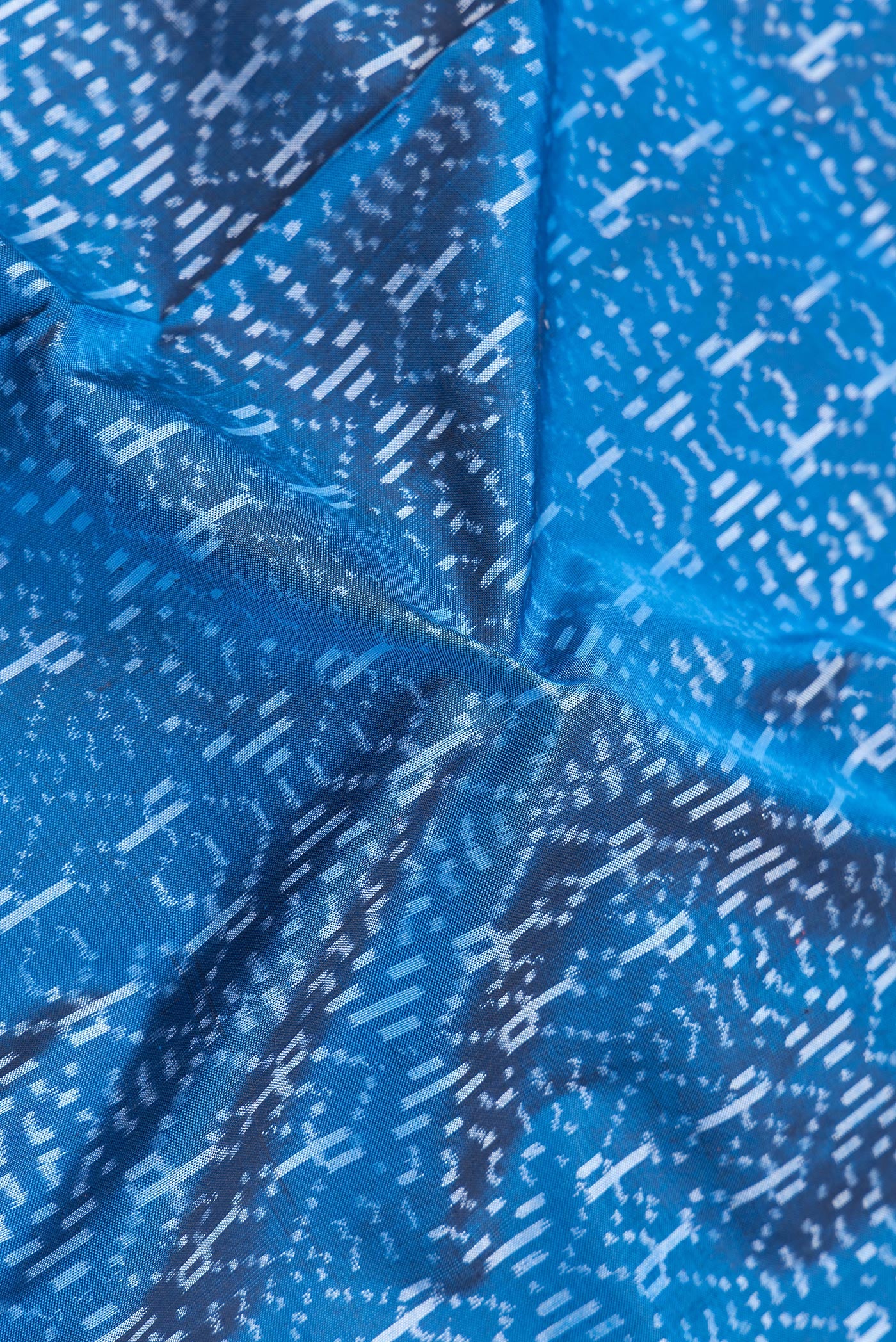 Close up of Peacock Blue Dual Tone Double Ikat Saree with Ikat Print on the body and Plain Border.  displaying folds