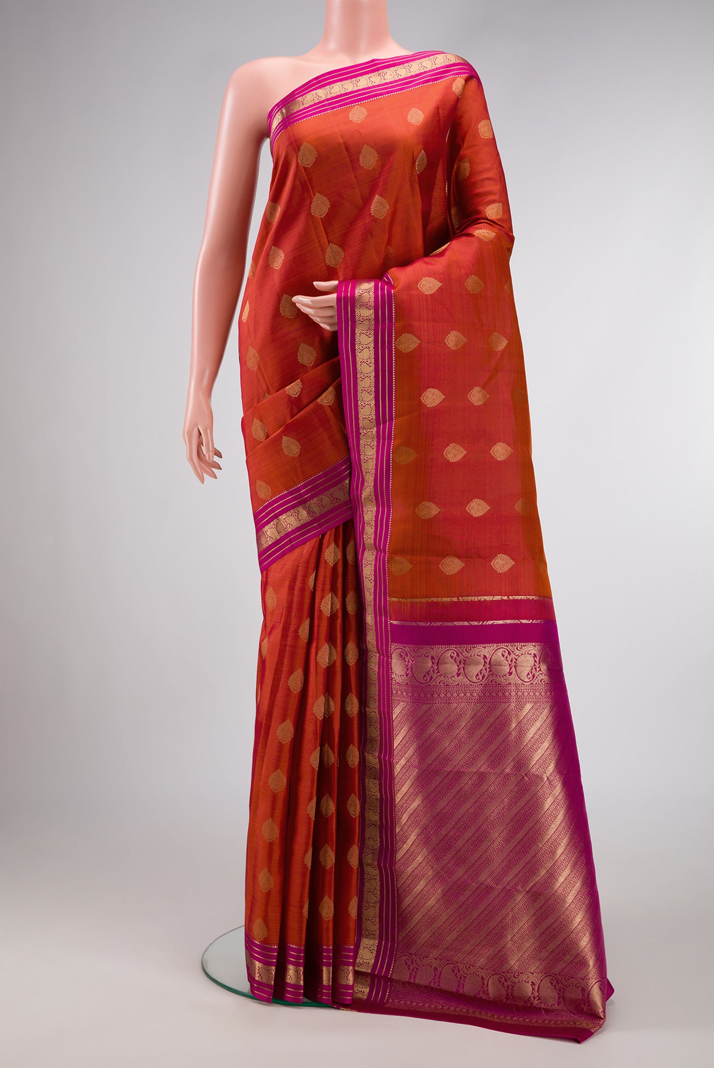 Brick Orange Dual Tone Kanchipuram Silk Saree with Zari Butta on the body and Thin Zari Line.  displayed on a mannequin