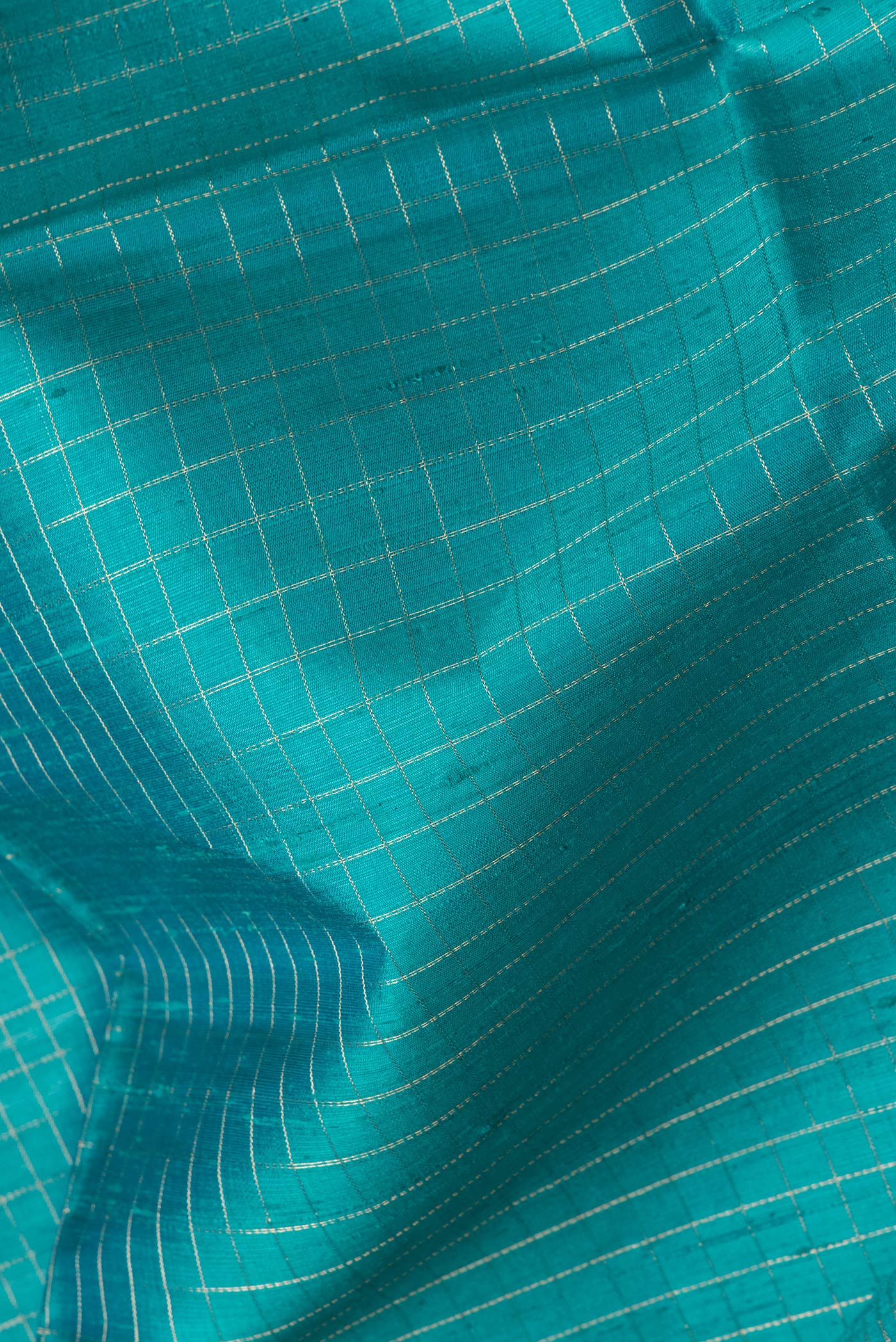 Close up of Peacock Blue Dual Tone Raw Silk Saree with Checked design on the body and Zari Border.  displaying folds