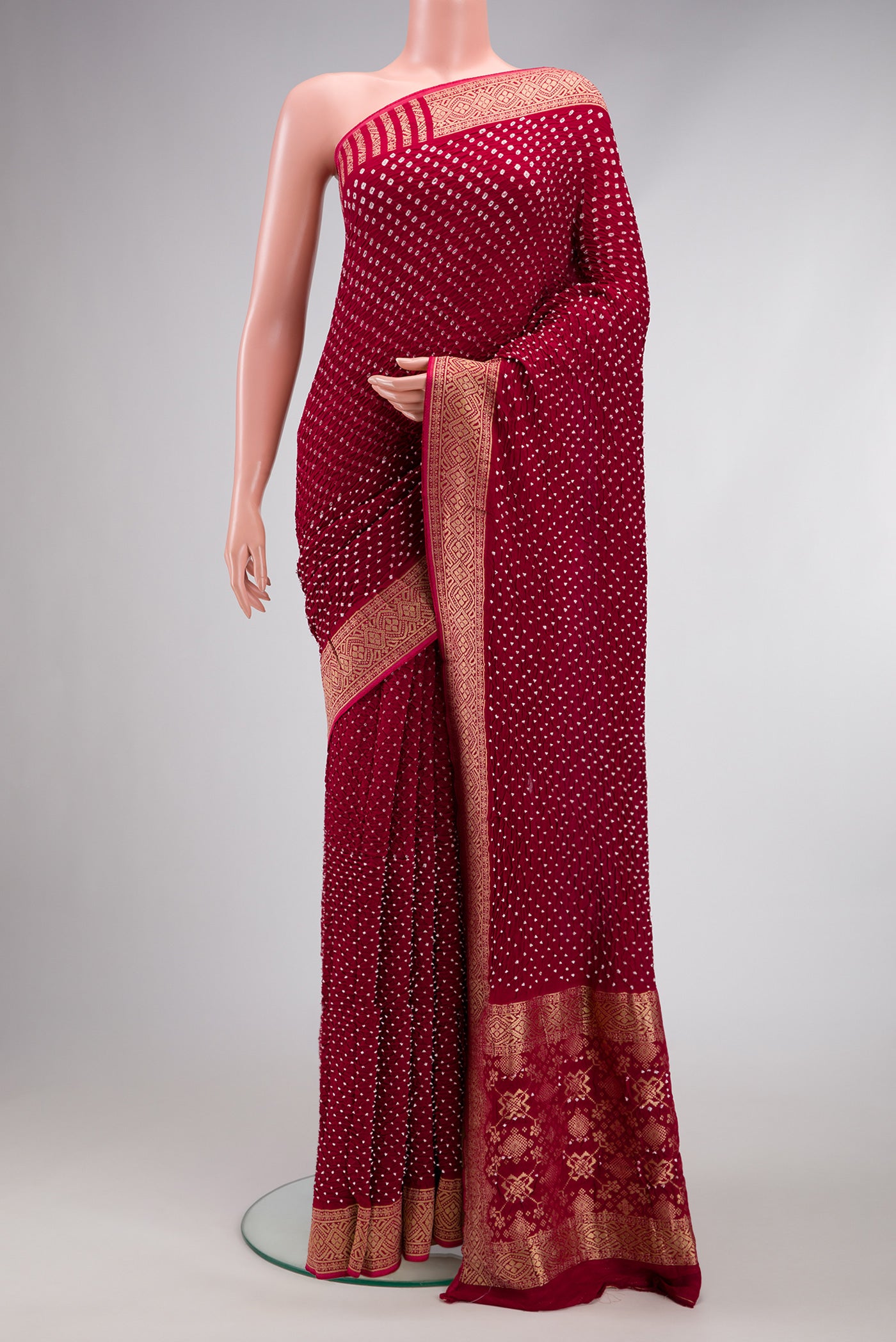 Maroon Bandhani Silk Saree with Bandhani Print on the body and Zari Border.  displayed on a mannequin