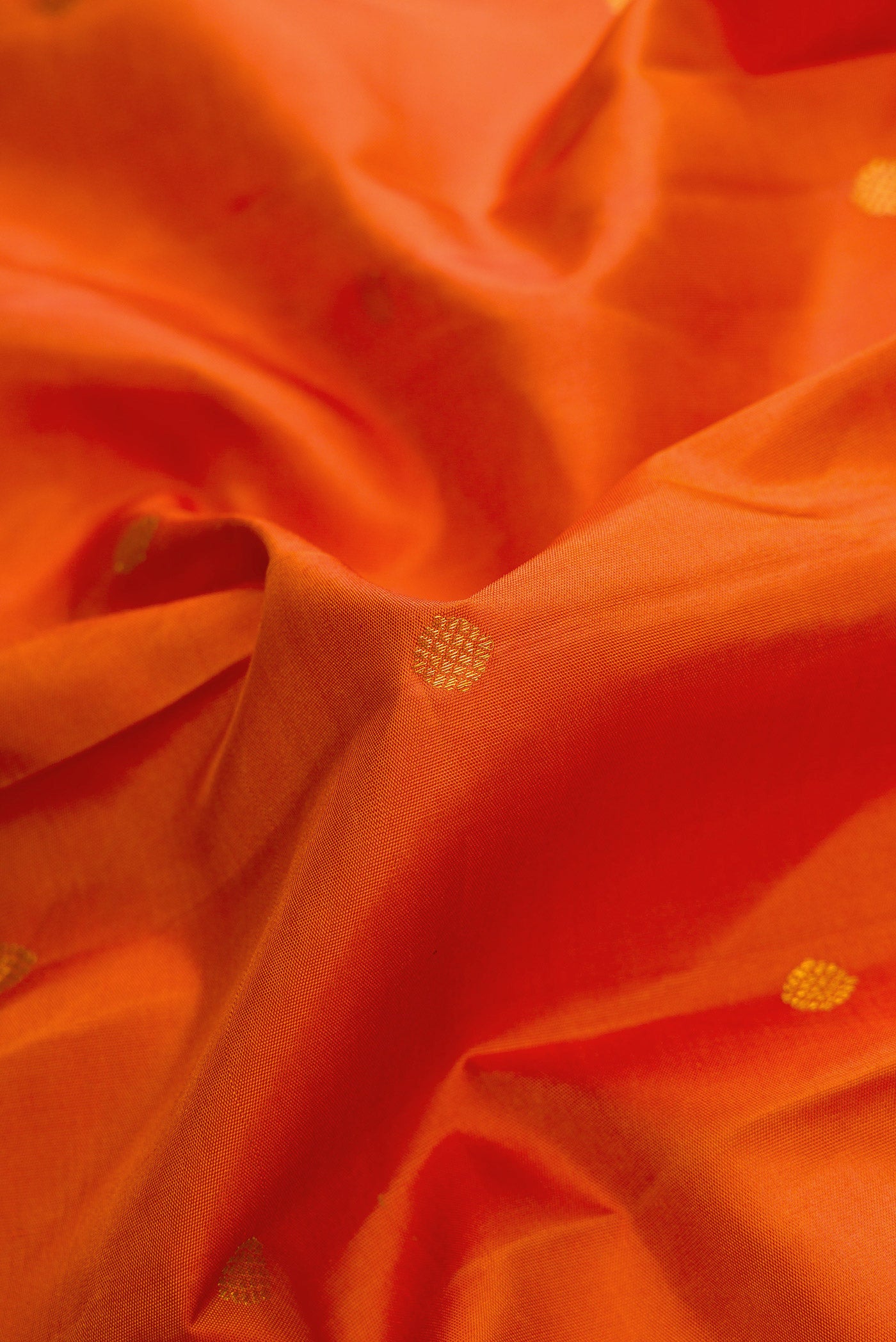 Close up of Pure Silk Pure Zari Brick Orange Dual Tone Kanjivaram Saree with Zari Butta on the body and Zari Border.  displaying folds