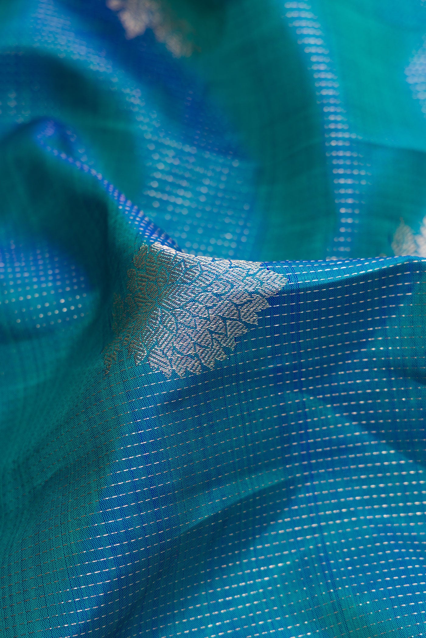 Close up of Peacock Blue Dual Tone Kanjivaram Silk Saree with Zari Butta on the body and Zari Border.  displaying folds