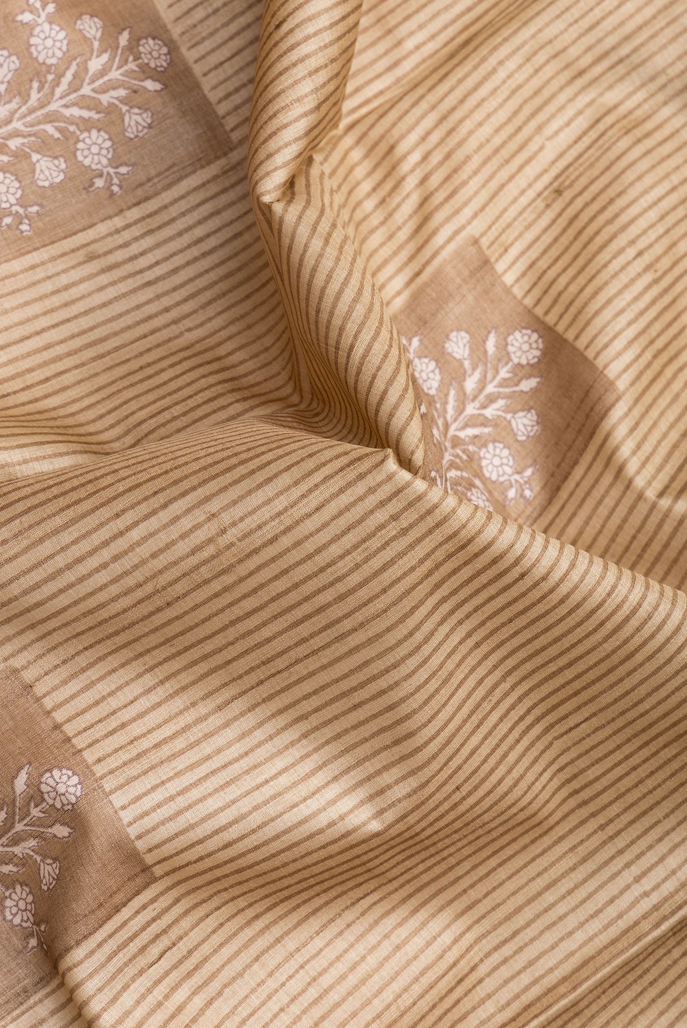Close up of Beige Tussar Silk Saree with Printed design on the body and Printed Border.  displaying folds