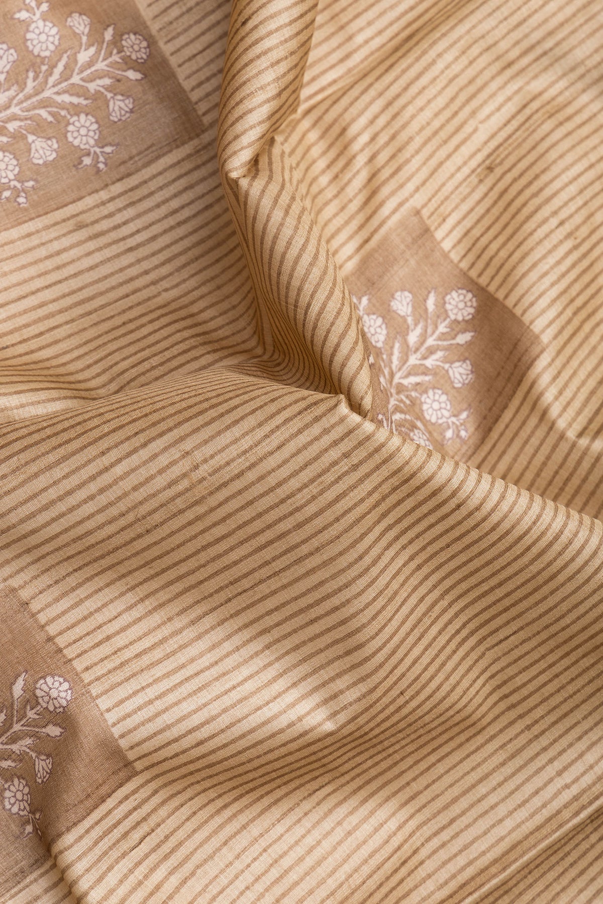 Close up of Beige Tussar Silk Saree with Printed design on the body and Printed Border.  displaying folds