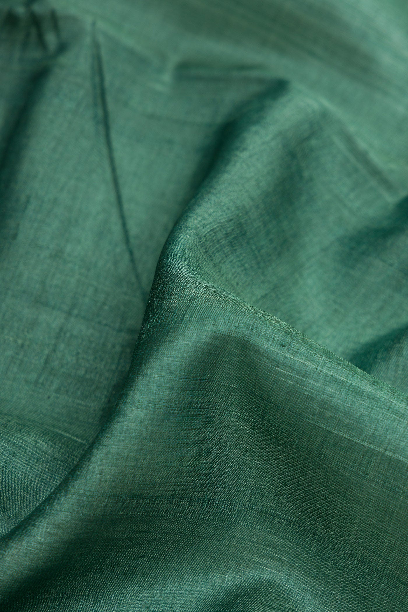 Close up of Green Dual Tone Tussar Silk Saree with Plain Body and Fancy Border.  displaying folds