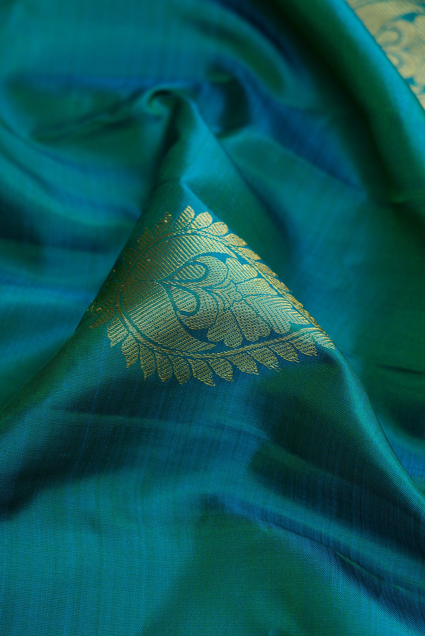 Close up of Peacock Blue Dual Tone Kanjivaram Silk Saree with Zari Butta on the body and Zari Border.  displaying folds