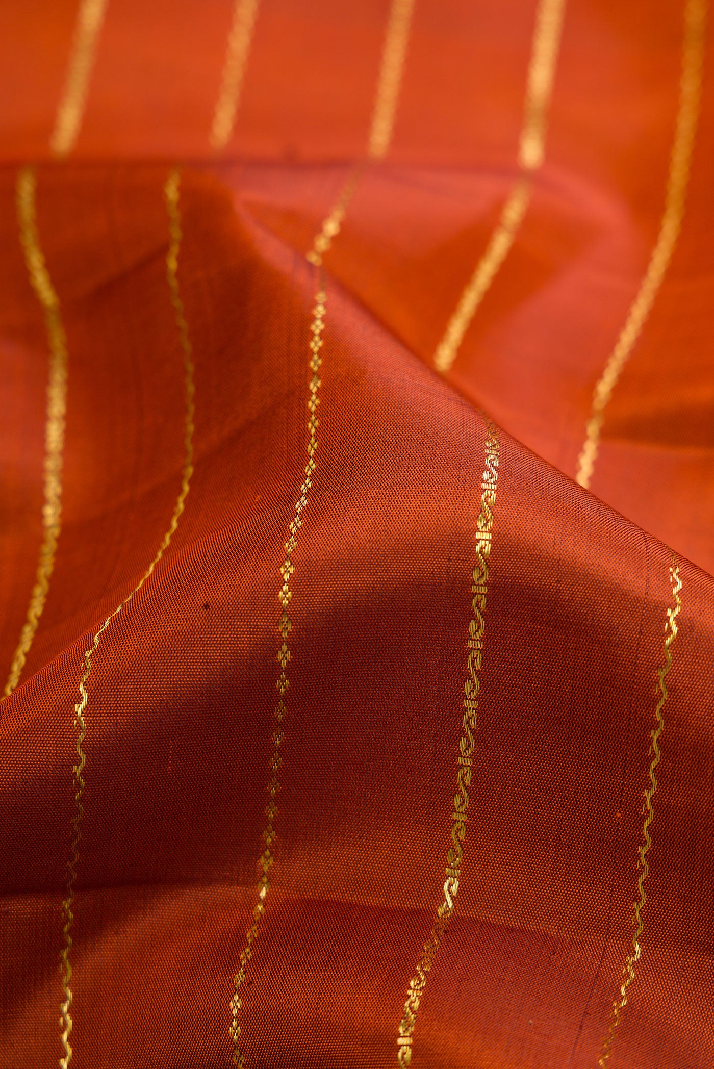 Close up of Brick Orange Dual Tone Kanchipuram Silk Saree with Stripes on the body and Zari Border.  displaying folds