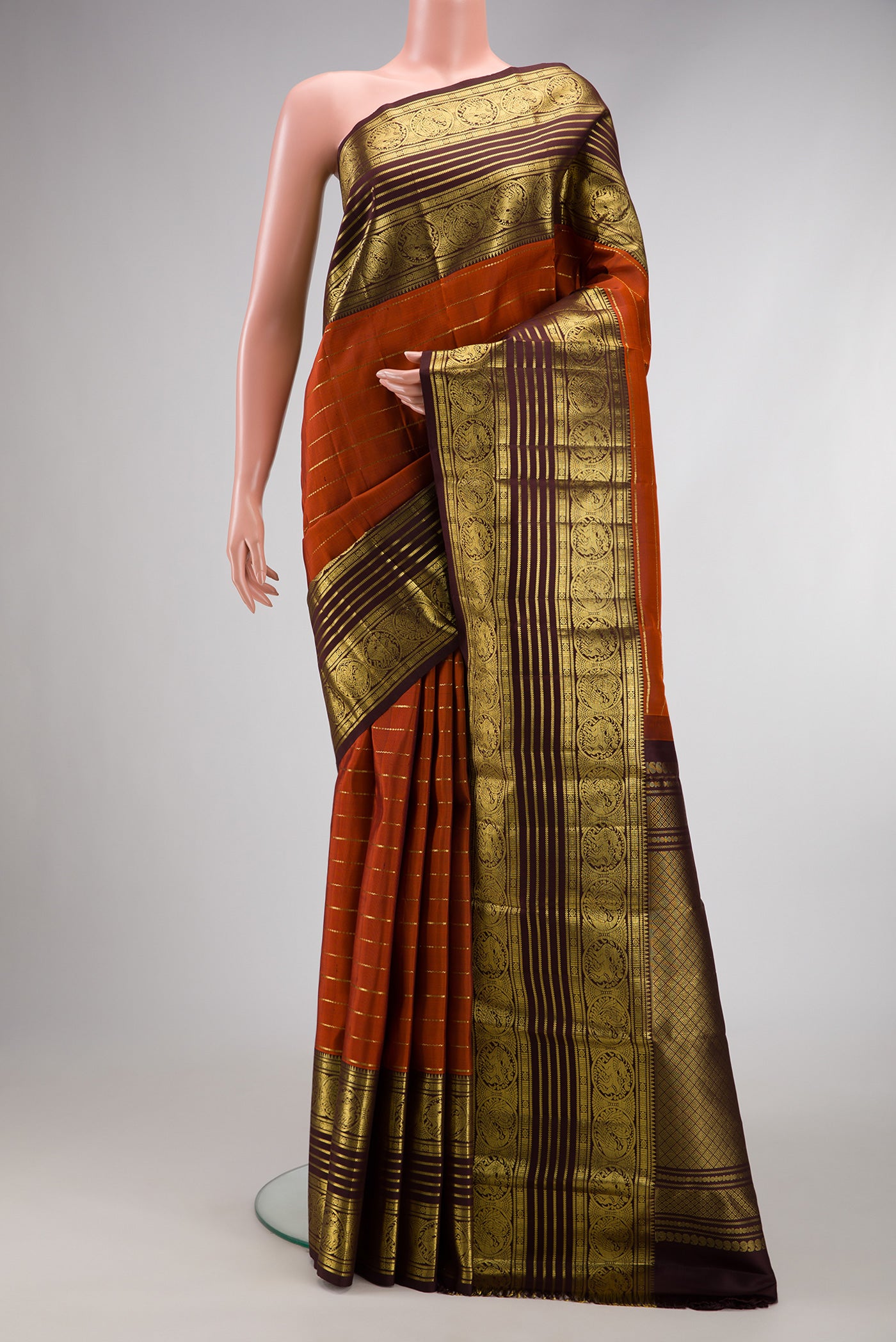 Brick Orange Dual Tone Kanchipuram Silk Saree with Stripes on the body and Zari Border.  displayed on a mannequin