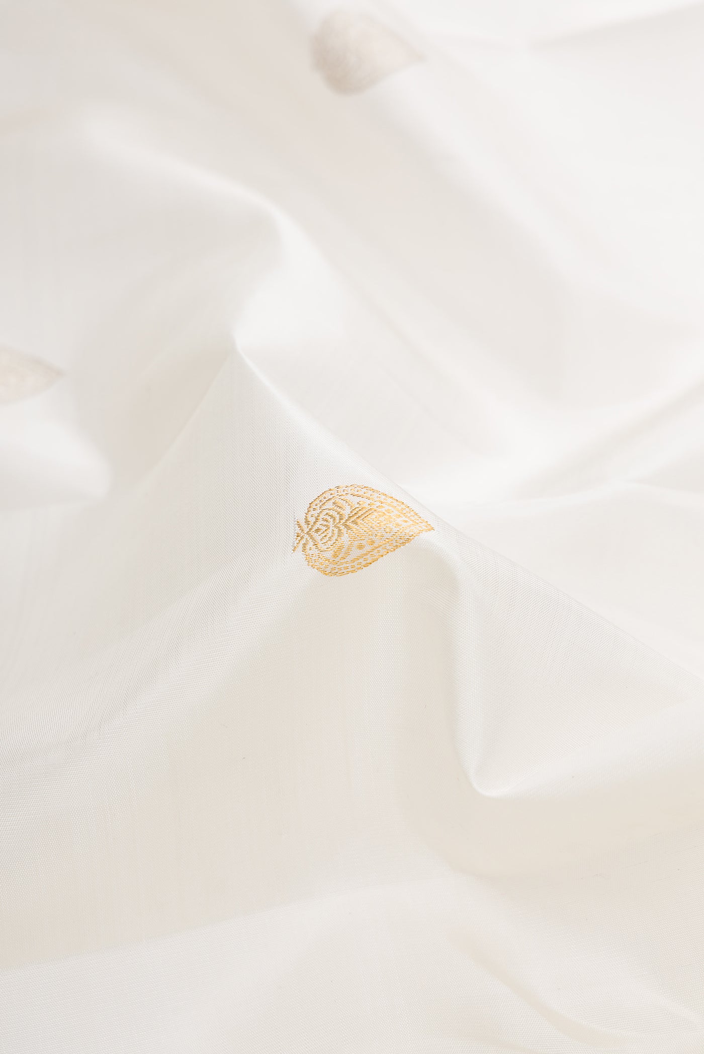 Close up of White Dual Tone Kanchipuram Silk Saree with Zari Butta on the body and Zari Border.  displaying folds