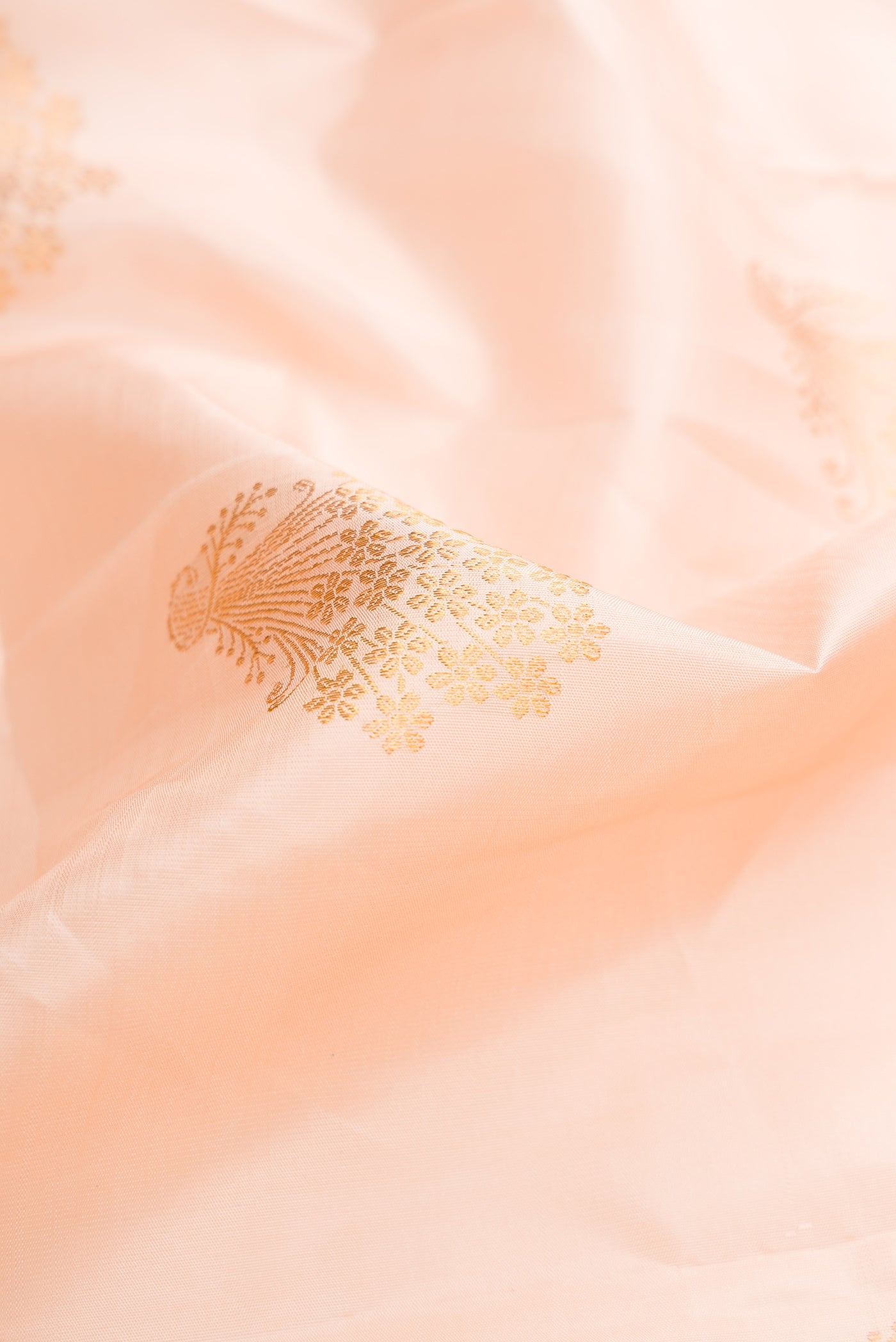 Close up of Peach Dual Tone Kanchipuram Silk Saree with Zari Butta on the body and Zari Border.  displaying folds
