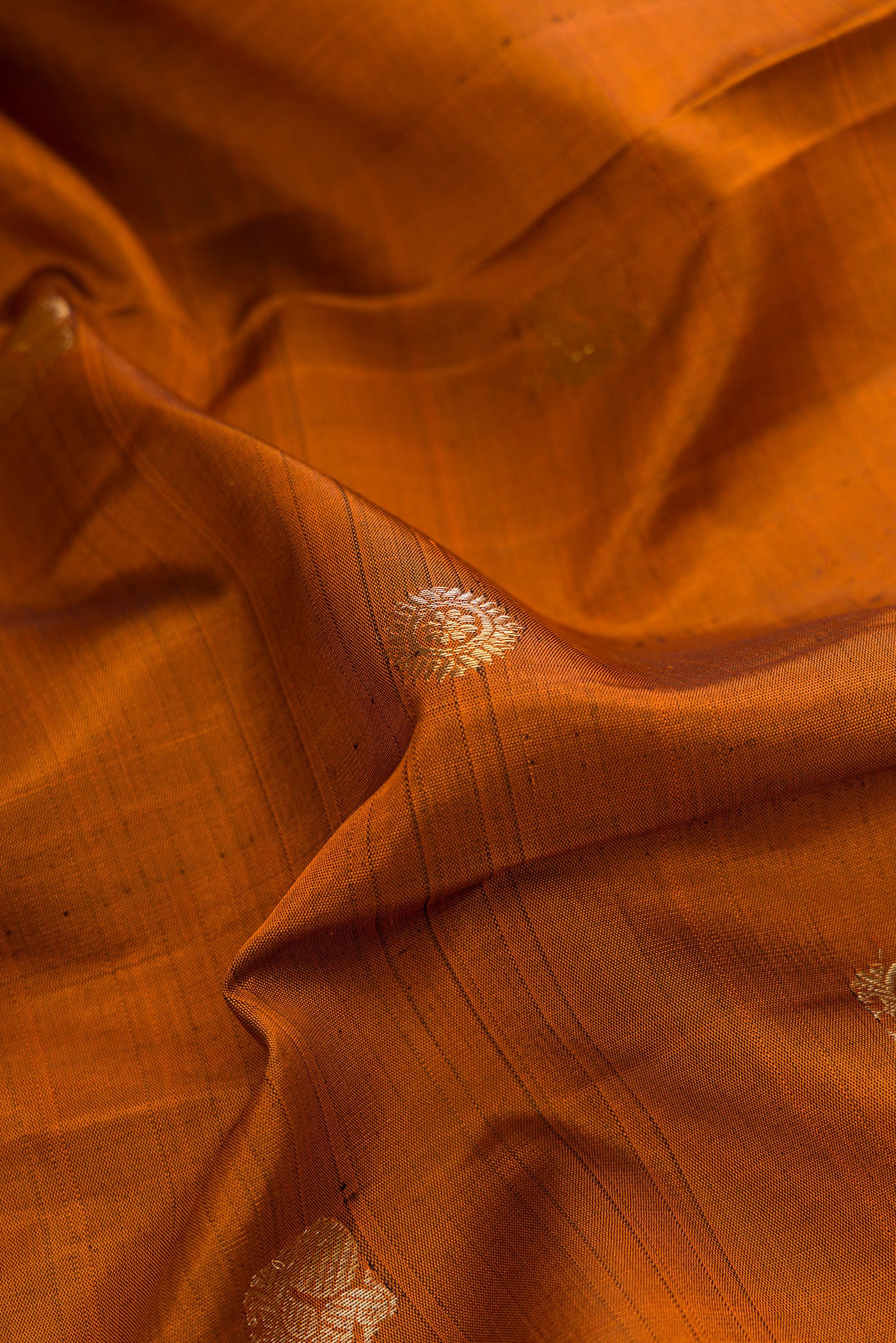 Close up of Brick Orange Dual Tone Kanjivaram Silk Saree with Zari Butta on the body and Ganga Jamuna Border.  displaying folds