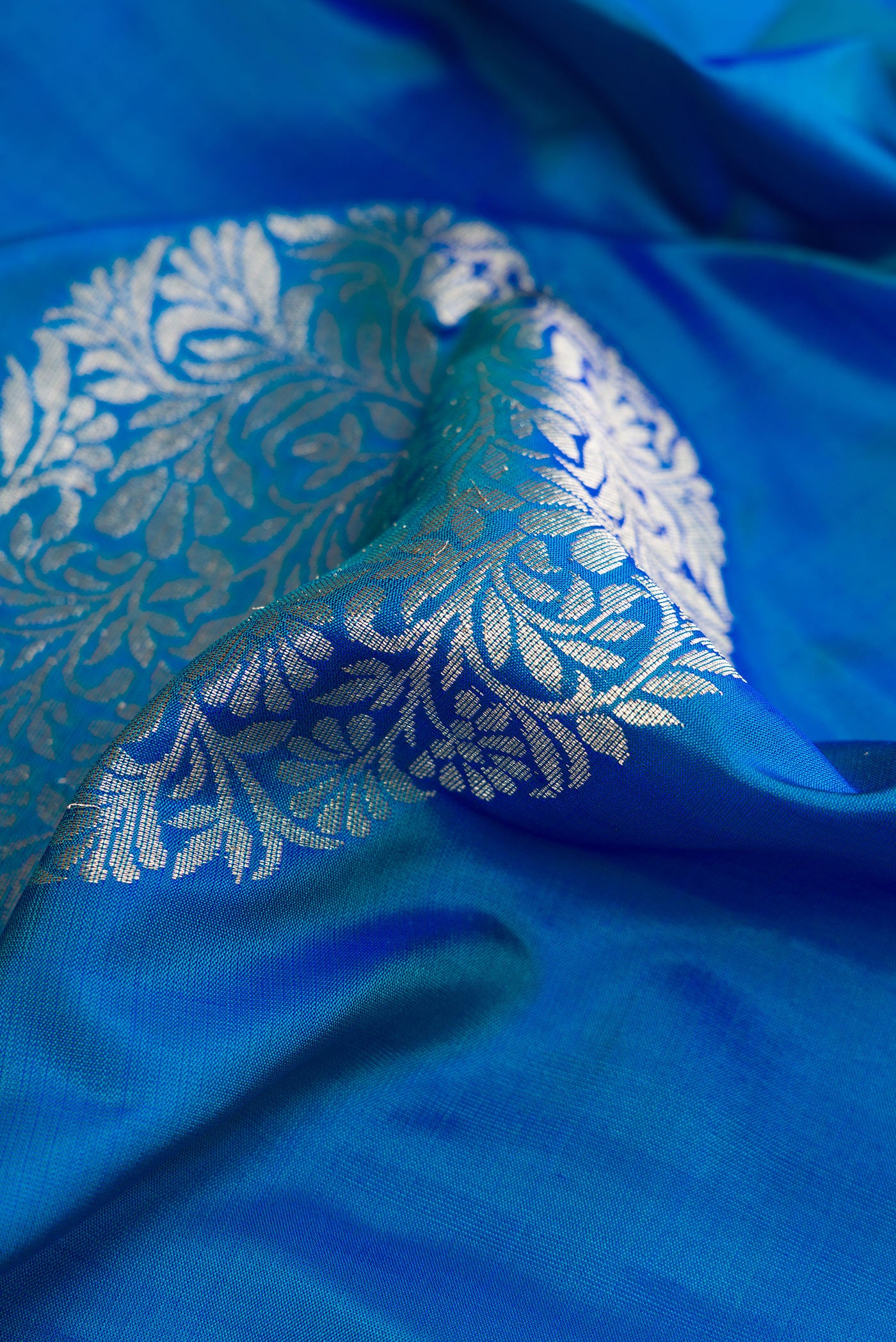 Close up of Peacock Blue Dual Tone Soft Silk Saree with Zari Butta on the body and Plain Border.  displaying folds