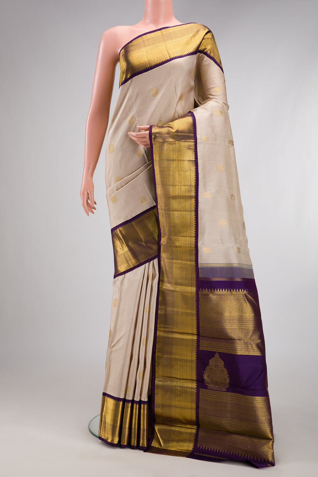 Beige Kanchipuram Silk Saree with Zari Butta on the body and Zari Border.  displayed on a mannequin