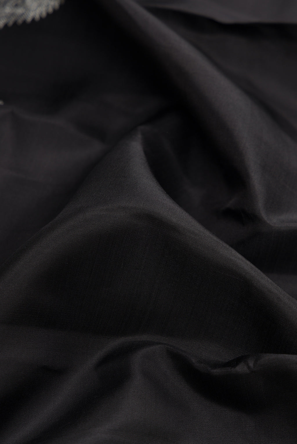 Close up of Black Dual Tone Kanjivaram Silk Saree with Plain Body and Fancy Border.  displaying folds