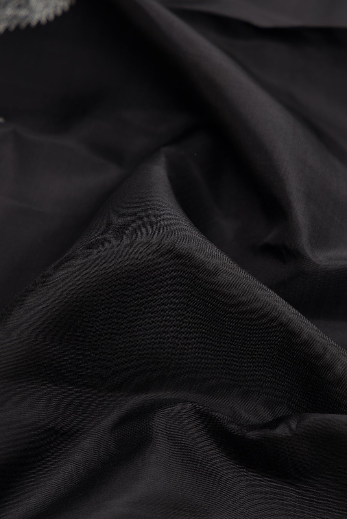 Close up of Black Dual Tone Kanjivaram Silk Saree with Plain Body and Fancy Border.  displaying folds
