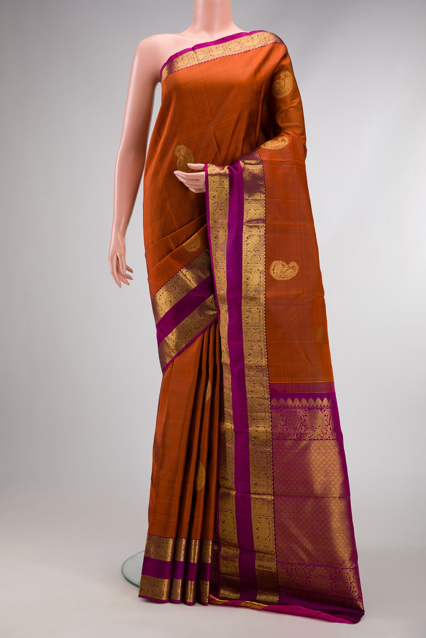 Brick Orange Kanjivaram Silk Saree with Zari Butta on the body and Zari Border.  displayed on a mannequin