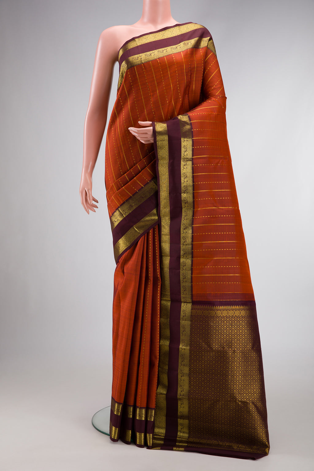 Brick Orange Dual Tone Kanjivaram Silk Saree with Stripes on the body and Zari Border.  displayed on a mannequin
