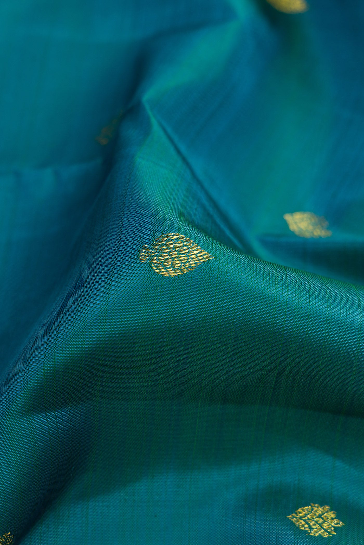 Close up of Teal Dual Tone Kanjivaram Silk Saree with Zari Butta on the body and Zari Border.  displaying folds