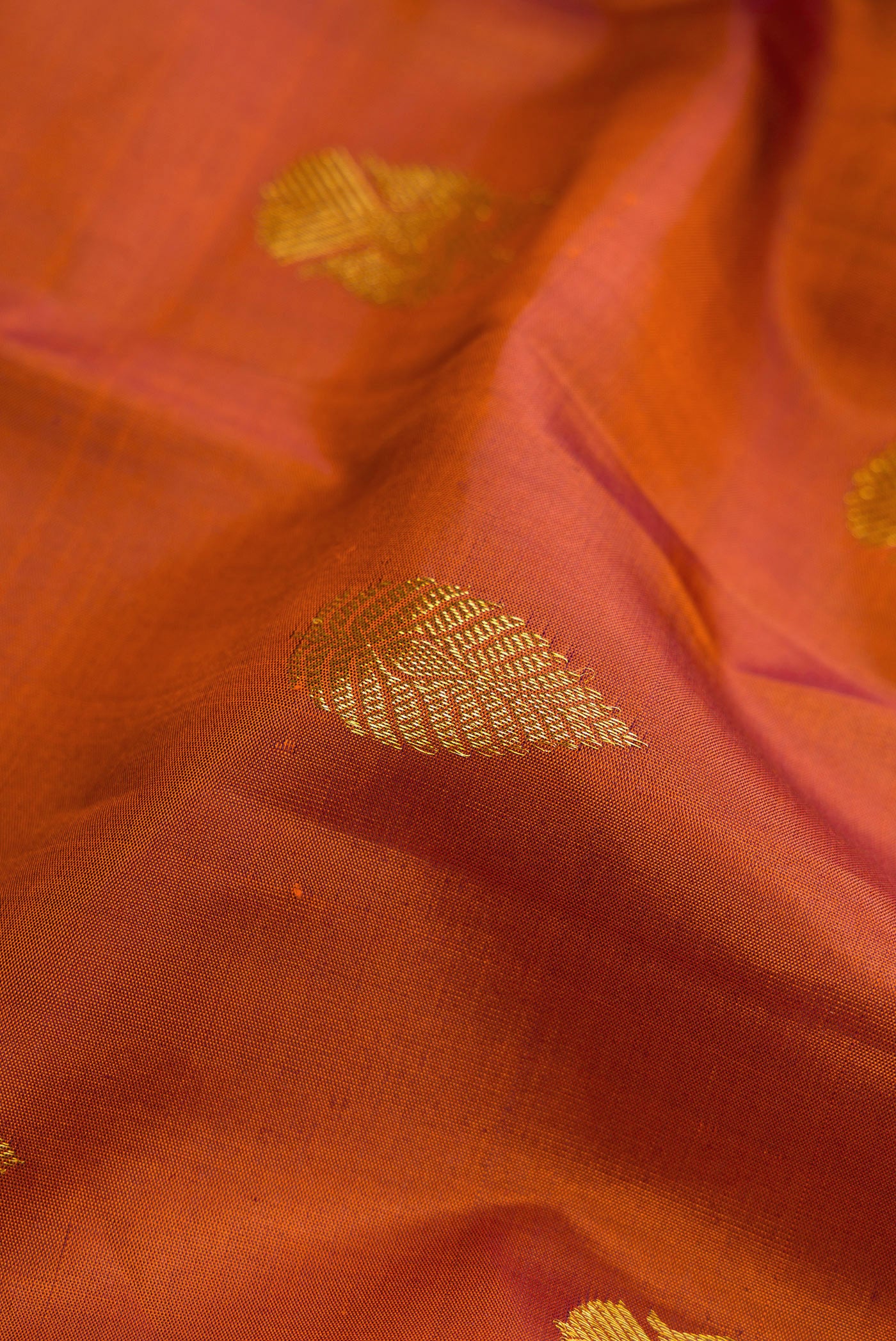 Close up of Brick Orange Dual Tone Kanjivaram Silk Saree with Zari Butta on the body and Zari Border.  displaying folds