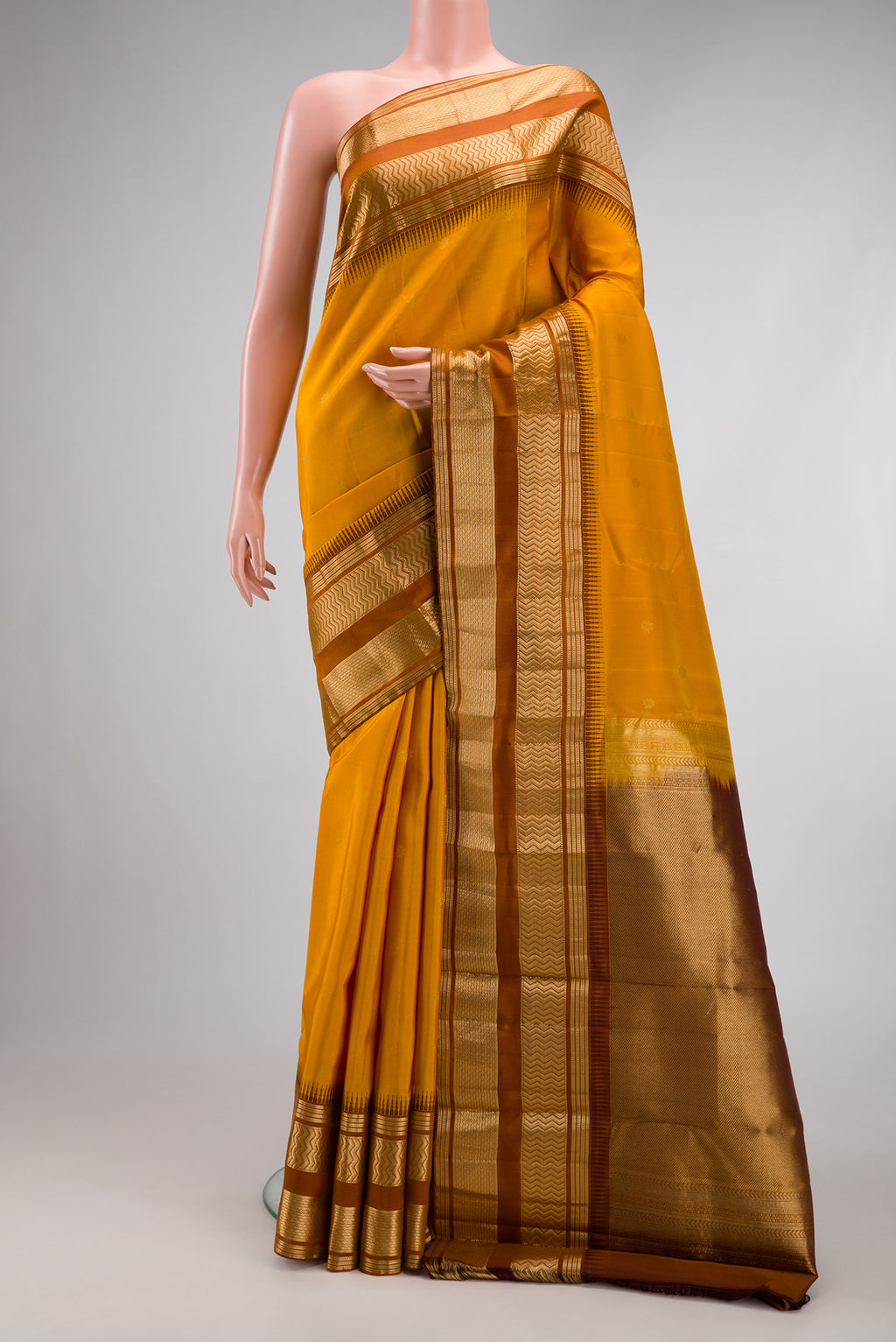 Mustard Kanjivaram Silk Saree with Zari Butta on the body and Zari Border.  displayed on a mannequin