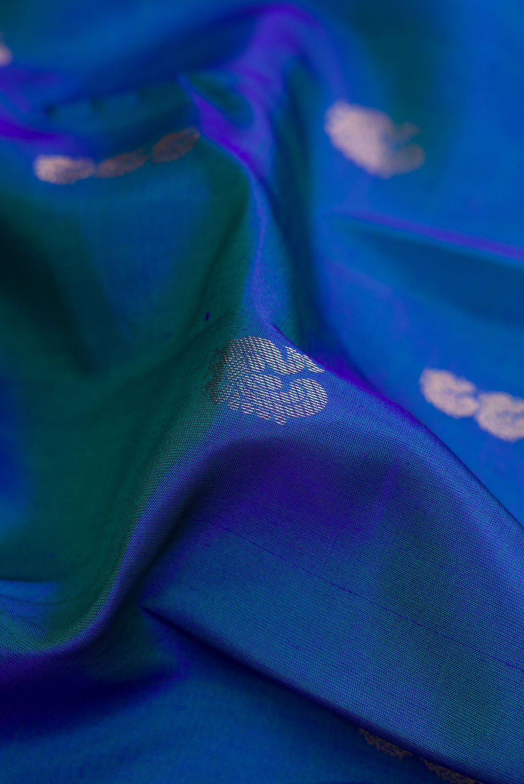 Close up of Peacock Blue Dual Tone Kanchipuram Silk Saree with Zari Butta on the body and Zari Border.  displaying folds