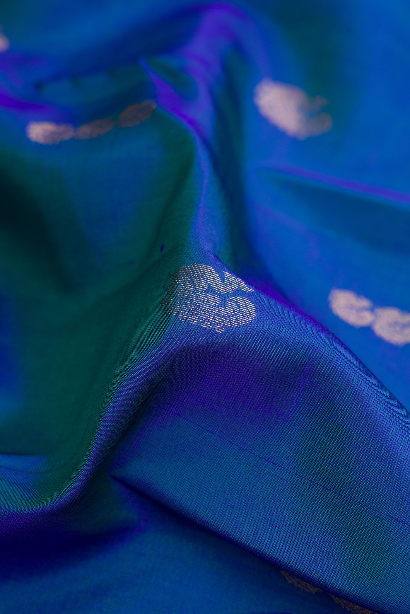 Close up of Peacock Blue Dual Tone Kanchipuram Silk Saree with Zari Butta on the body and Zari Border.  displaying folds