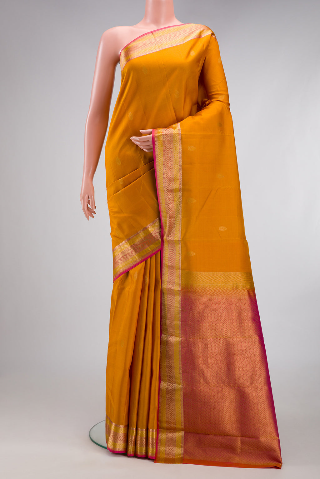 Mustard Kanchipuram Silk Saree with Zari Butta on the body and Zari Border.  displayed on a mannequin