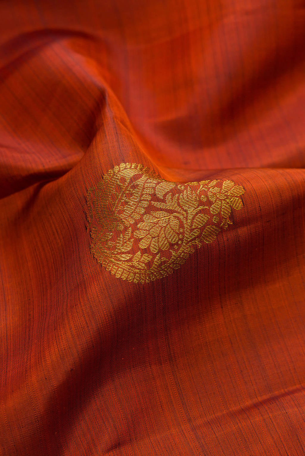 Close up of Brick Orange Kanjivaram Silk Saree with Zari Butta on the body and Zari Border.  displaying folds