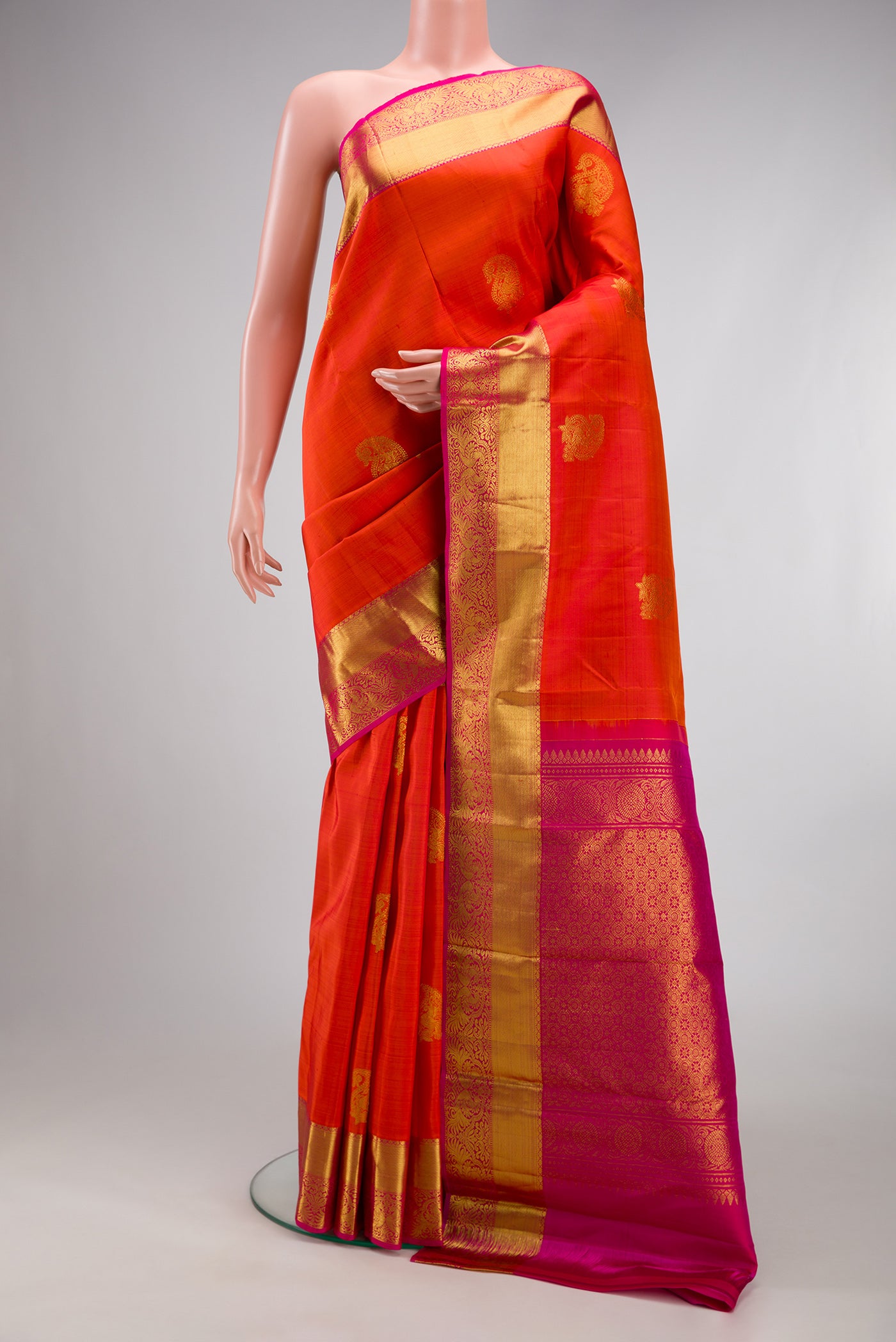 Orange Kanjivaram Silk Saree with Zari Butta on the body and Zari Border.  displayed on a mannequin