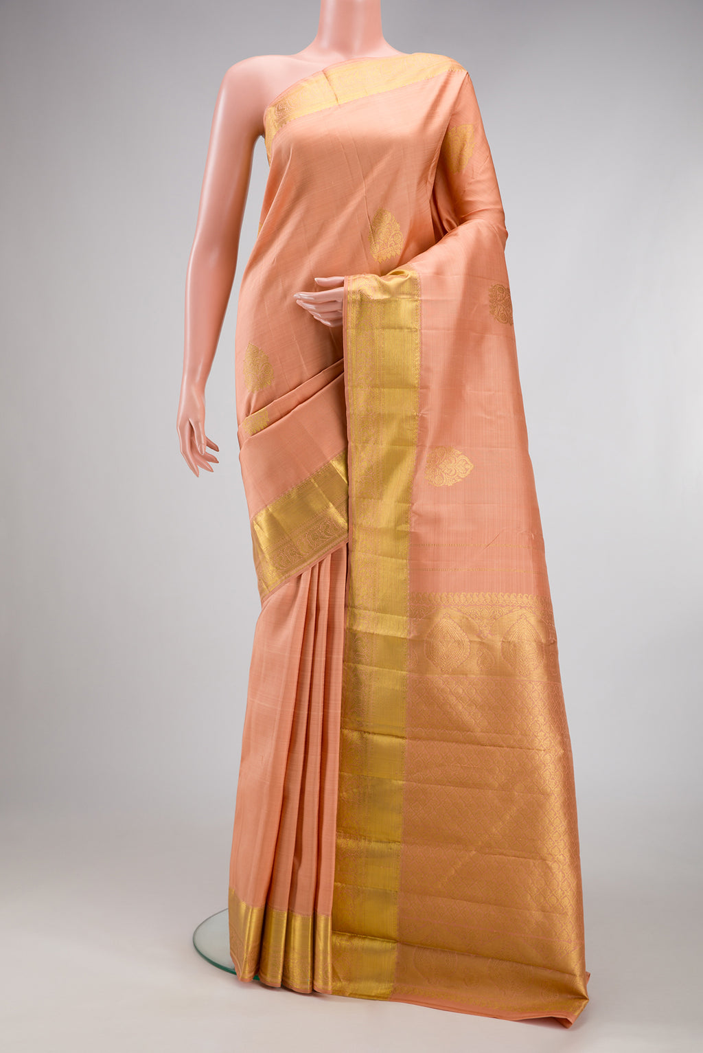 Peach Kanjivaram Silk Saree with Zari Butta on the body and Zari Border.  displayed on a mannequin