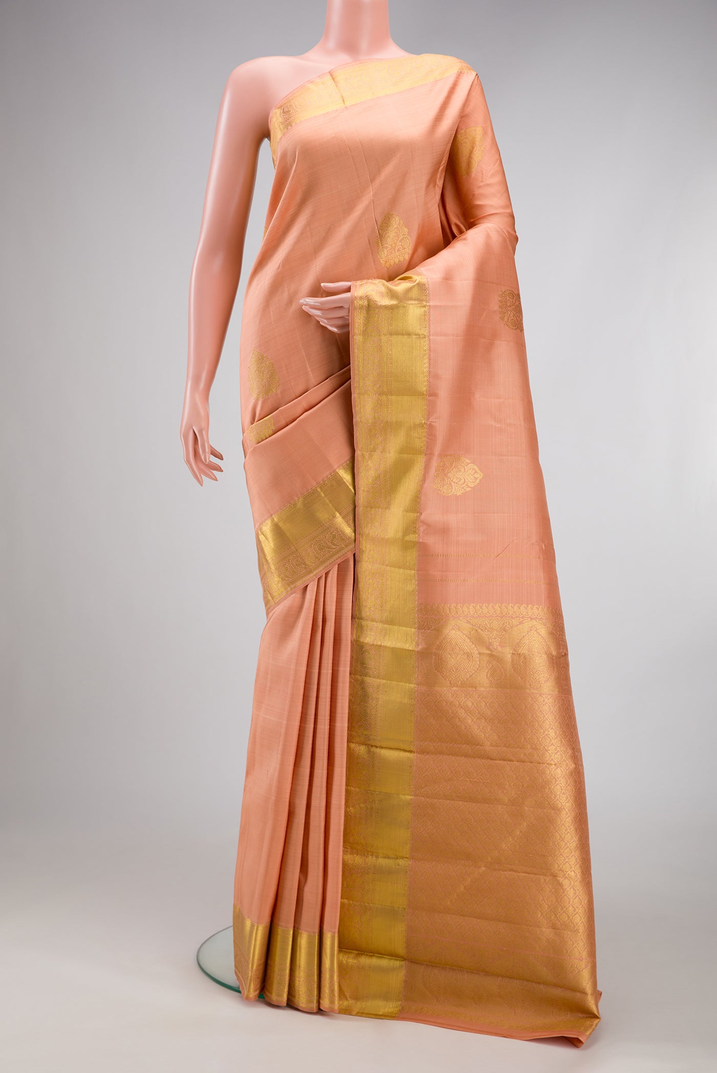 Peach Kanjivaram Silk Saree with Zari Butta on the body and Zari Border.  displayed on a mannequin