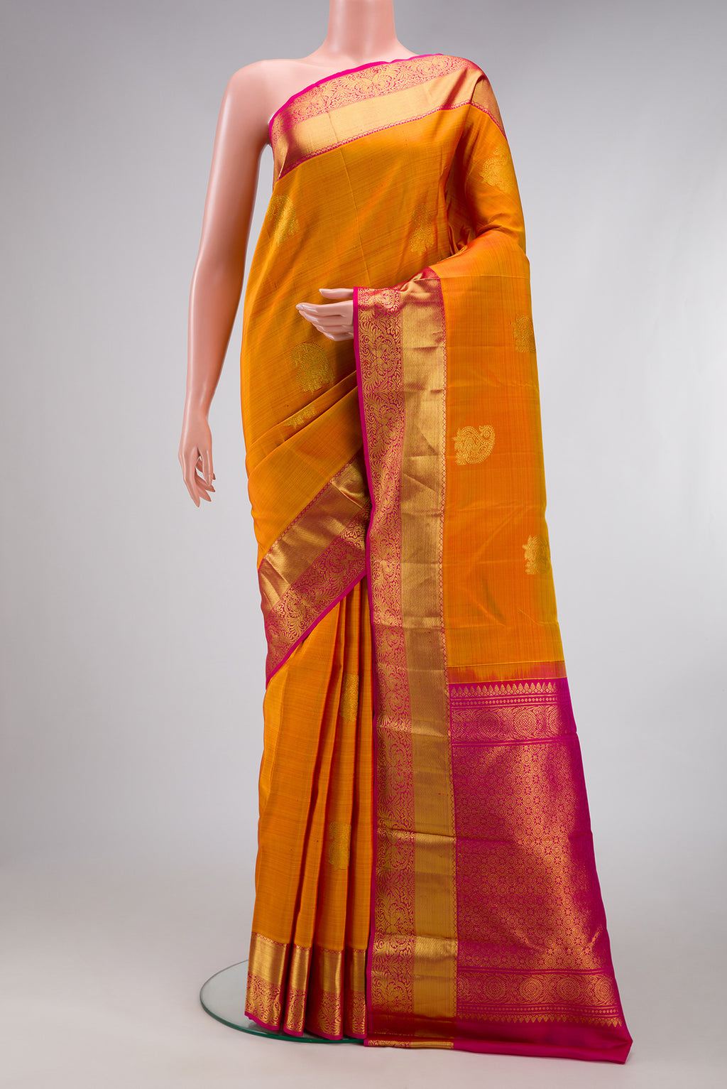 Mustard Kanjivaram Silk Saree with Zari Butta on the body and Zari Border.  displayed on a mannequin