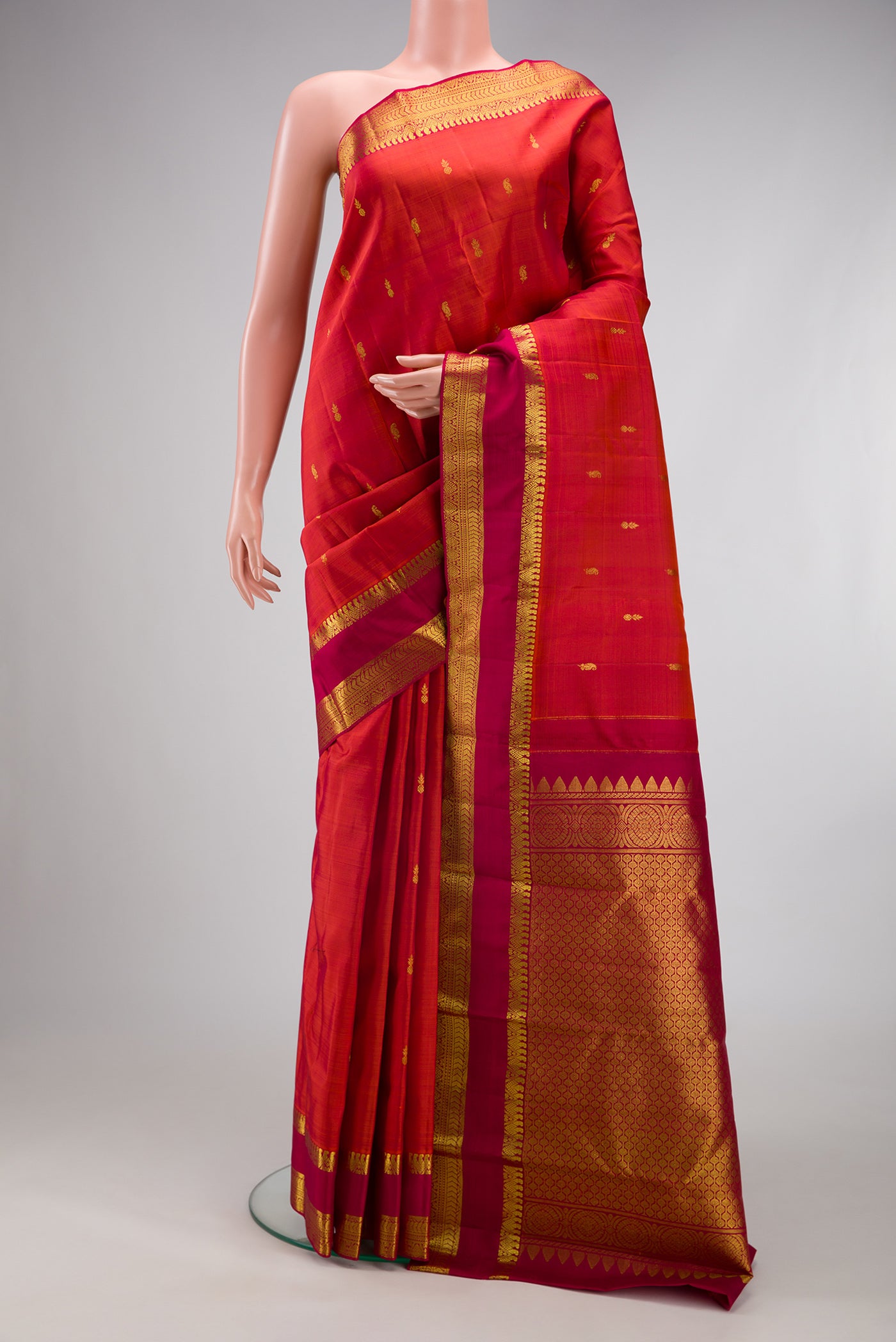 Brick Orange Kanjivaram Silk Saree with Zari Butta on the body and Zari Border.  displayed on a mannequin