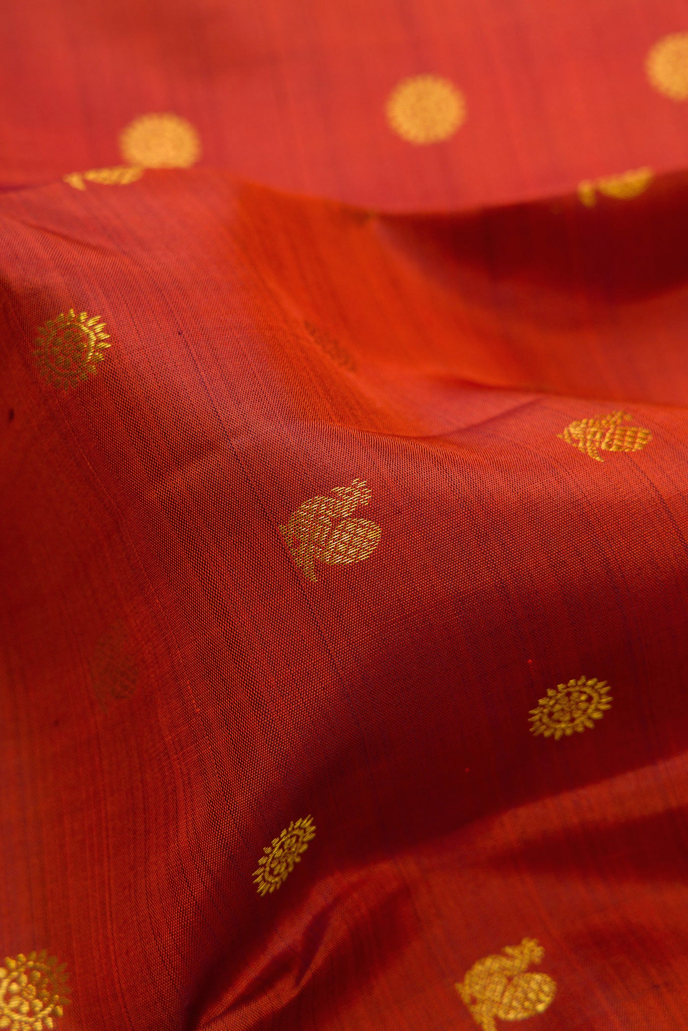 Close up of Rust Kanjivaram Silk Saree with Zari Butta on the body and Zari Border.  displaying folds