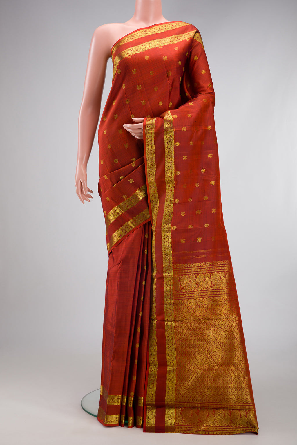 Rust Kanjivaram Silk Saree with Zari Butta on the body and Zari Border.  displayed on a mannequin
