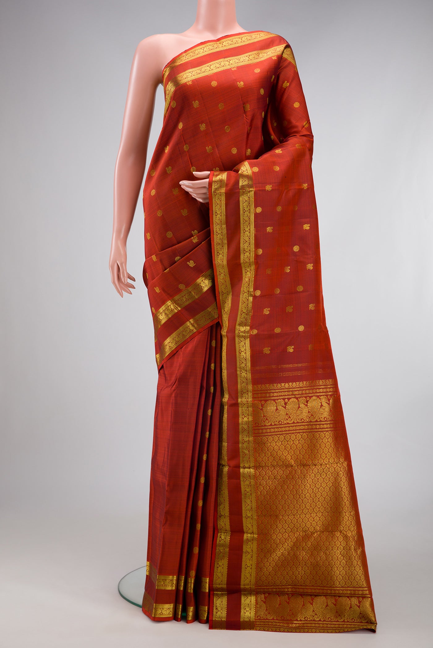 Rust Kanjivaram Silk Saree with Zari Butta on the body and Zari Border.  displayed on a mannequin