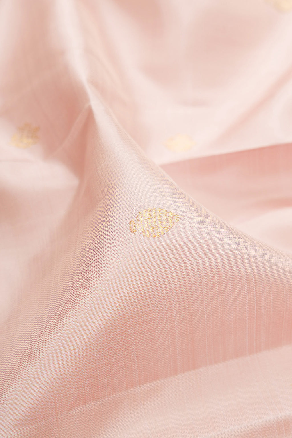 Close up of Rose Gold Kanjivaram Silk Saree with Zari Butta on the body and Zari Border.  displaying folds