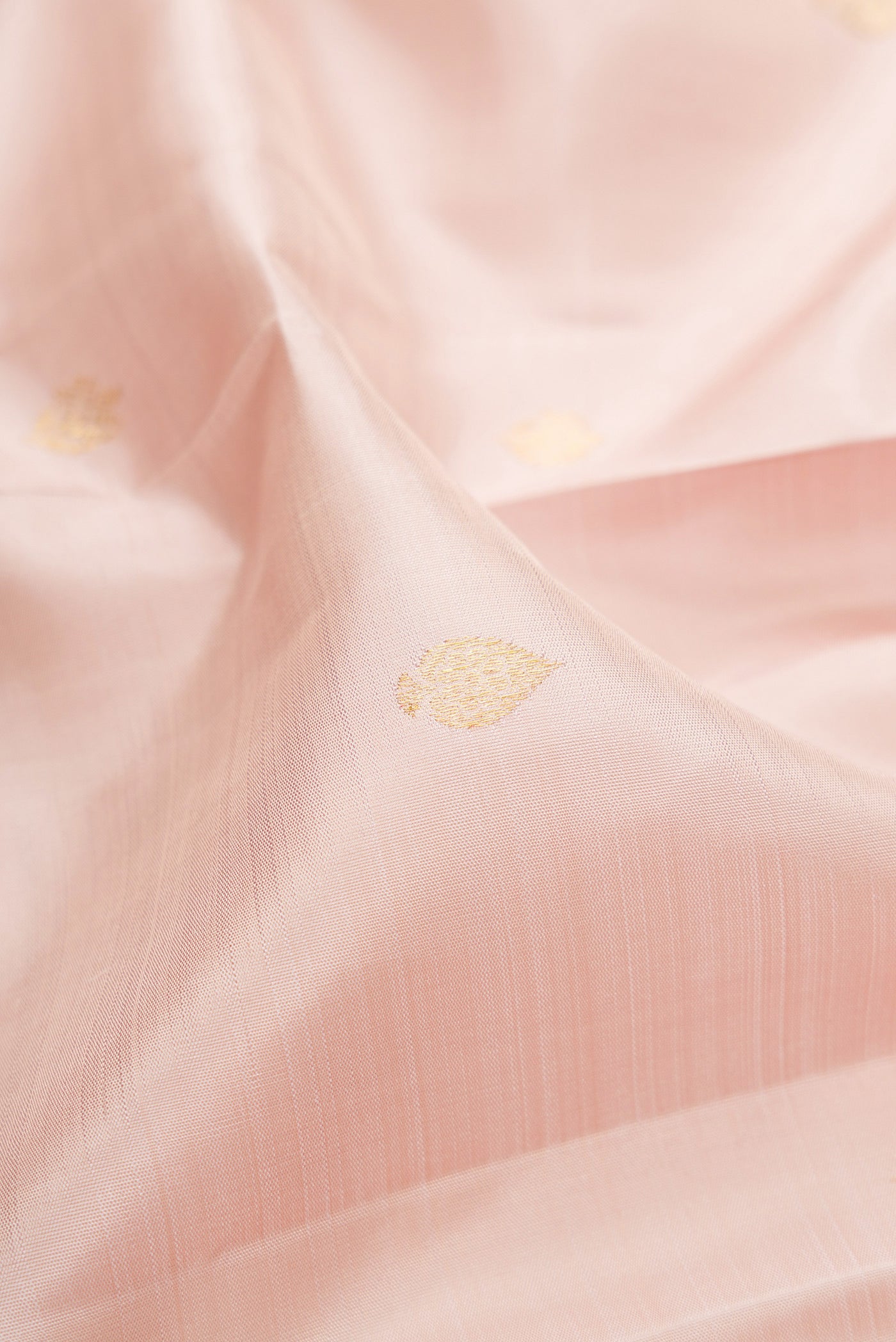 Close up of Rose Gold Kanjivaram Silk Saree with Zari Butta on the body and Zari Border.  displaying folds