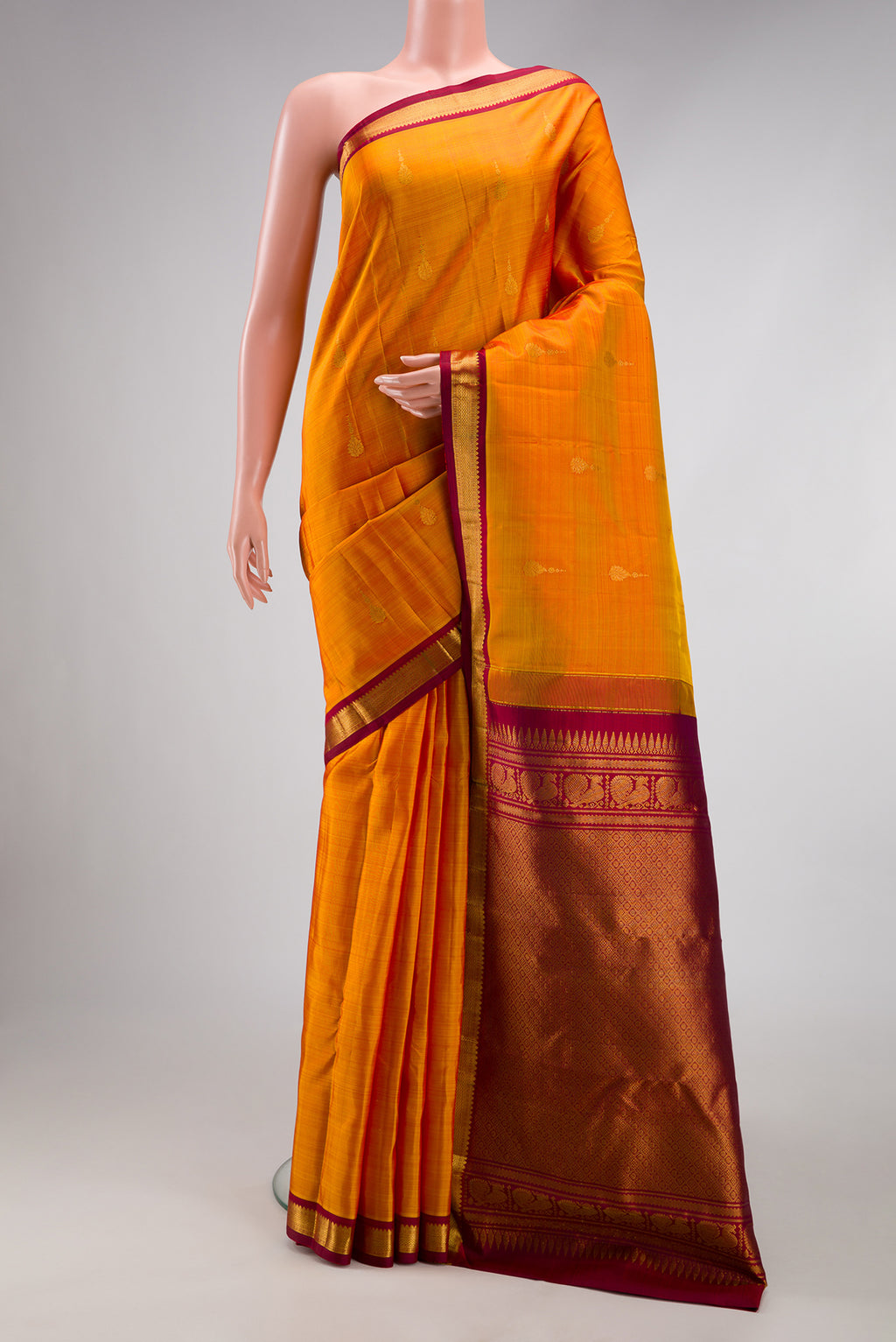Mustard Kanchipuram Silk Saree with Zari Butta on the body and Zari Border.  displayed on a mannequin