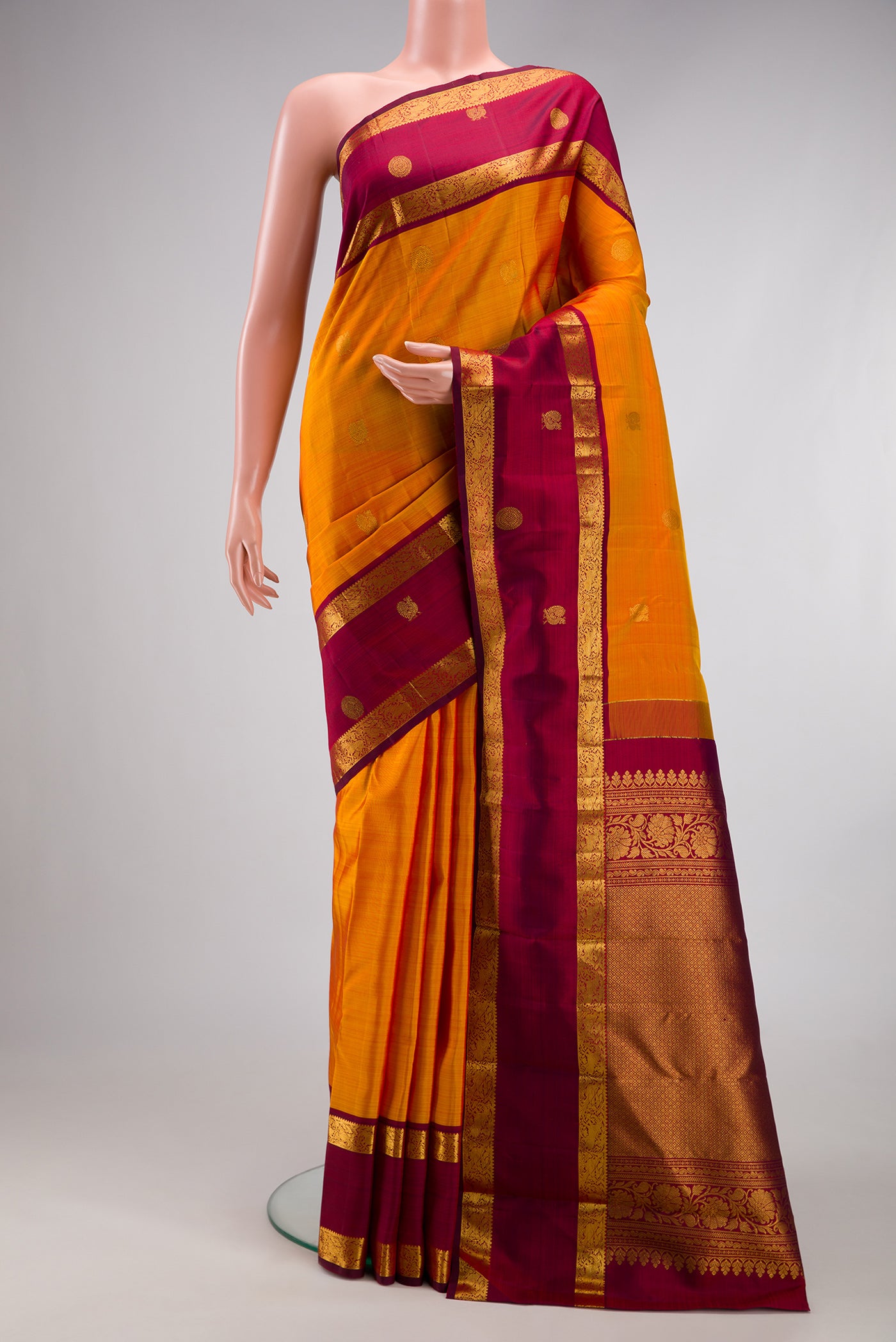 Mustard Kanjivaram Silk Saree with Zari Butta on the body and Zari Border.  displayed on a mannequin